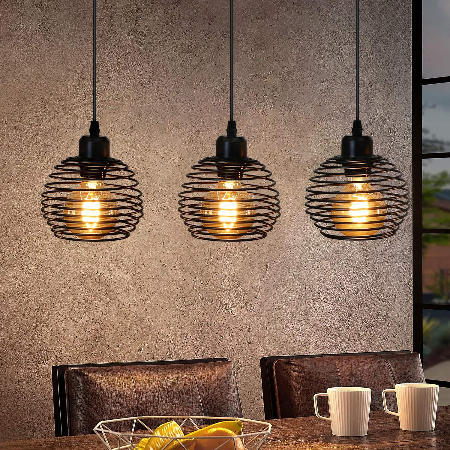 Drei schwarze Pendelleuchten mit Wendeldesign und leuchtenden Glühbirnen über einem Tisch mit Objekten.
