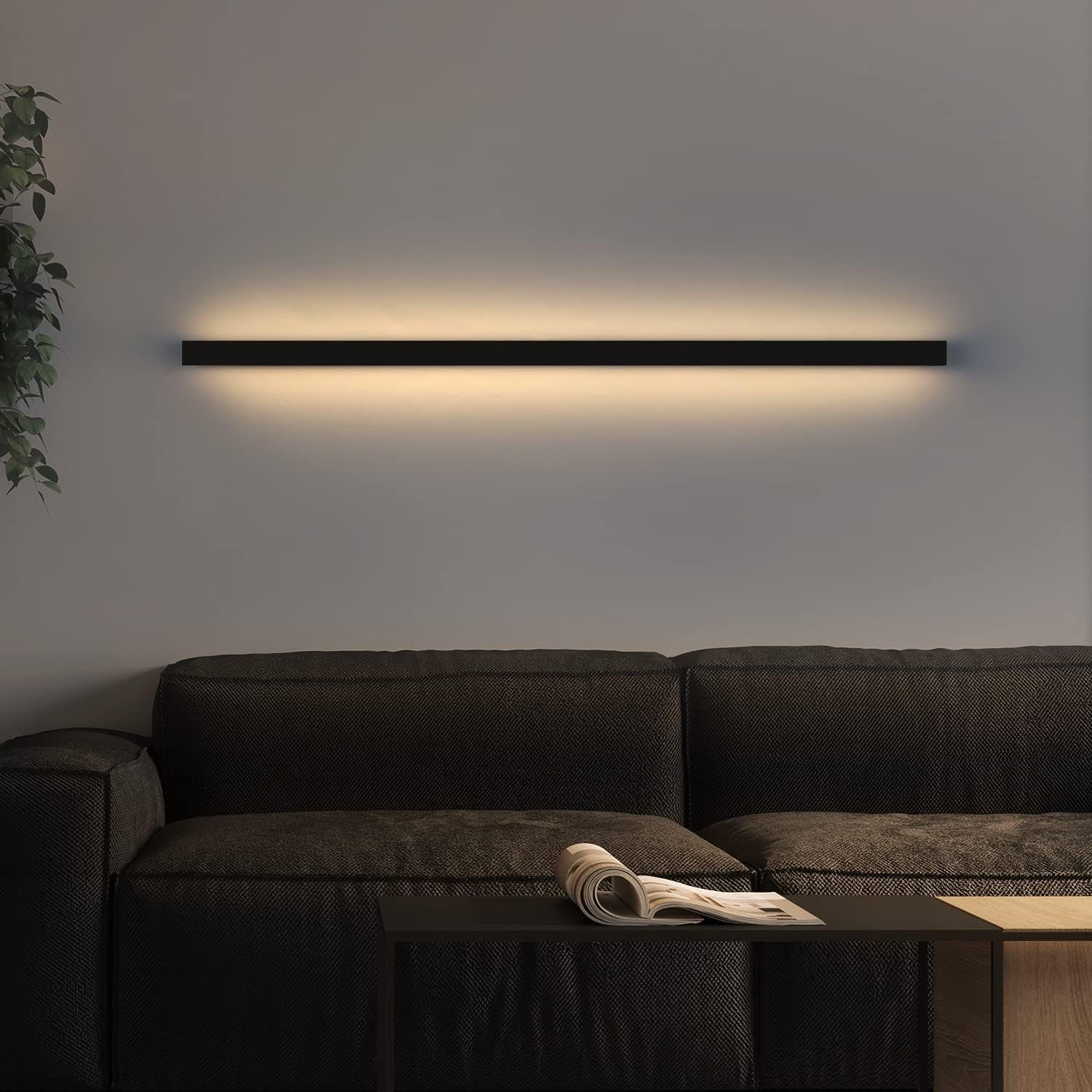 Ein schwarzes, horizontales LED-Licht ist an einer grauen Wand über einem schwarzen Sofa montiert.