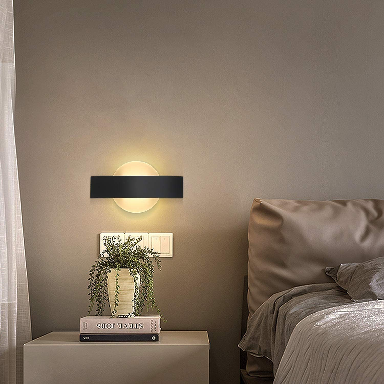 Lampa ścienna z czarną ramą i okrągłym światłem. Na zdjęciu widoczna jest roślina i łóżko.