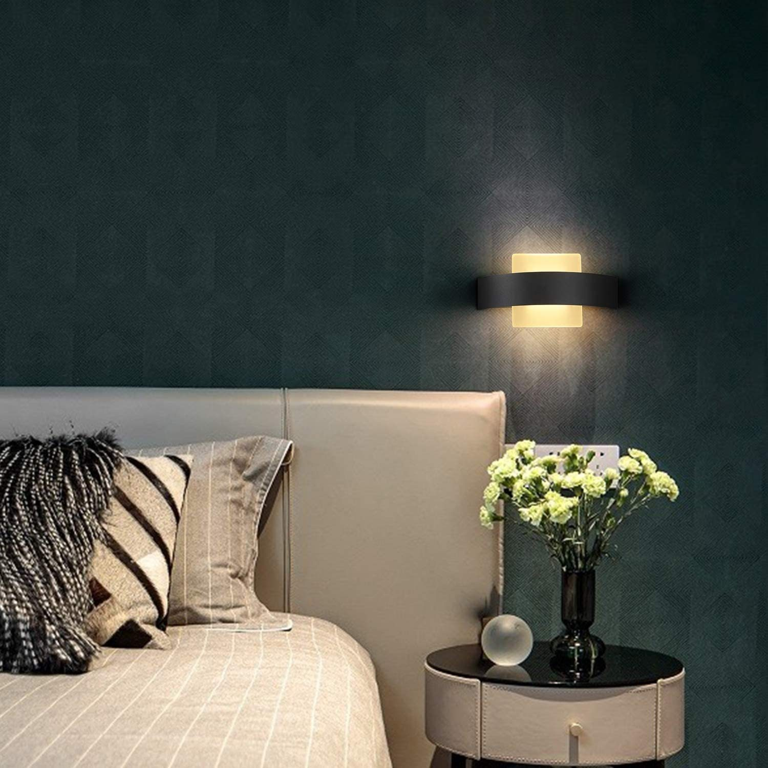 Camera da letto con lampada a parete sopra il letto e vaso di fiori sul tavolo.