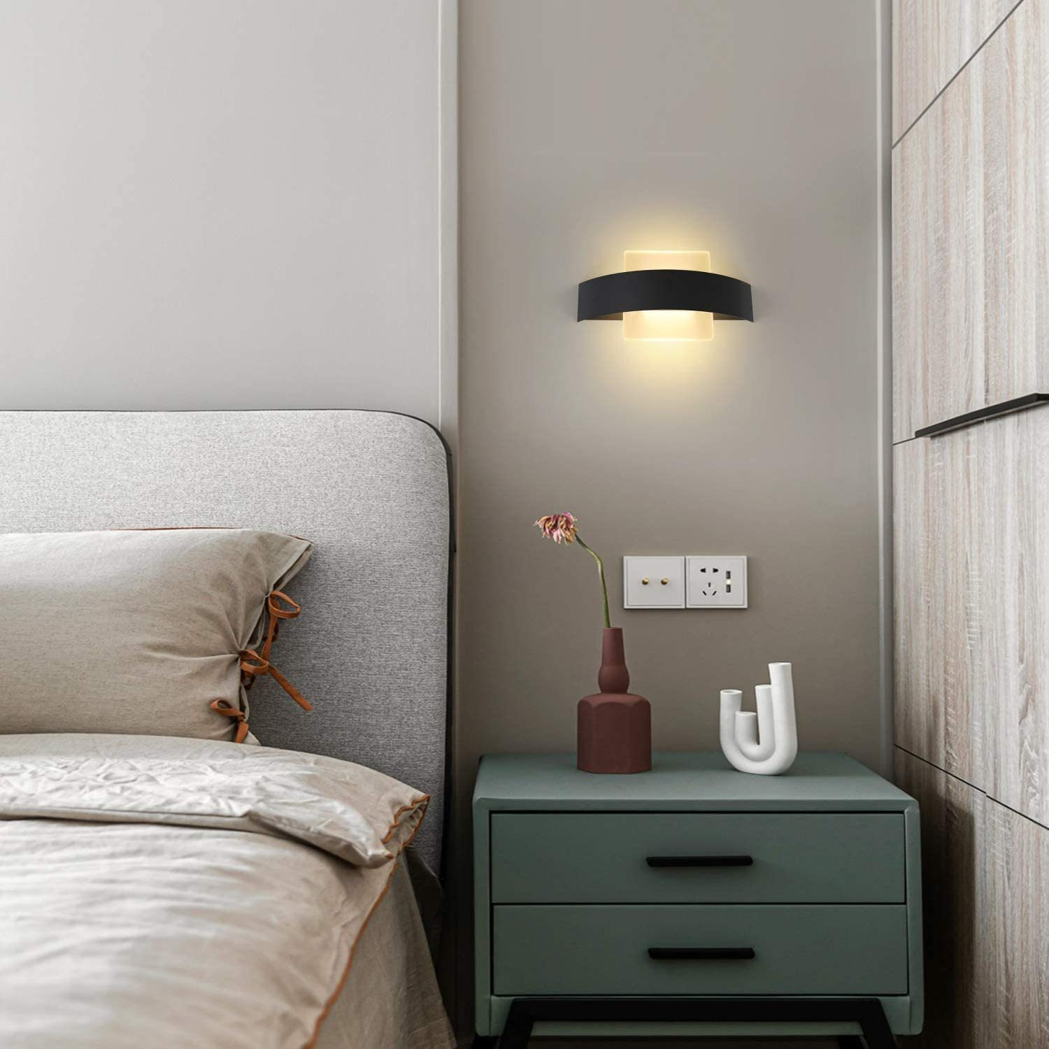 Wandlampe an einer Wand neben einem Bett und einem Schrank. Vase mit Blumen auf dem Schrank.