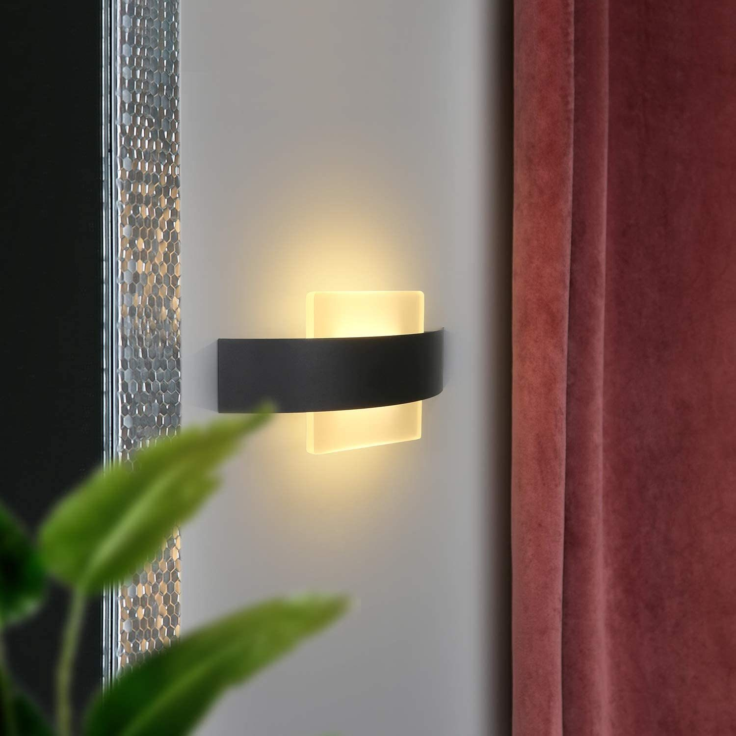 Una moderna lampada da parete. È nera e ha una luce che brilla da dietro un pannello rettangolare bianco.