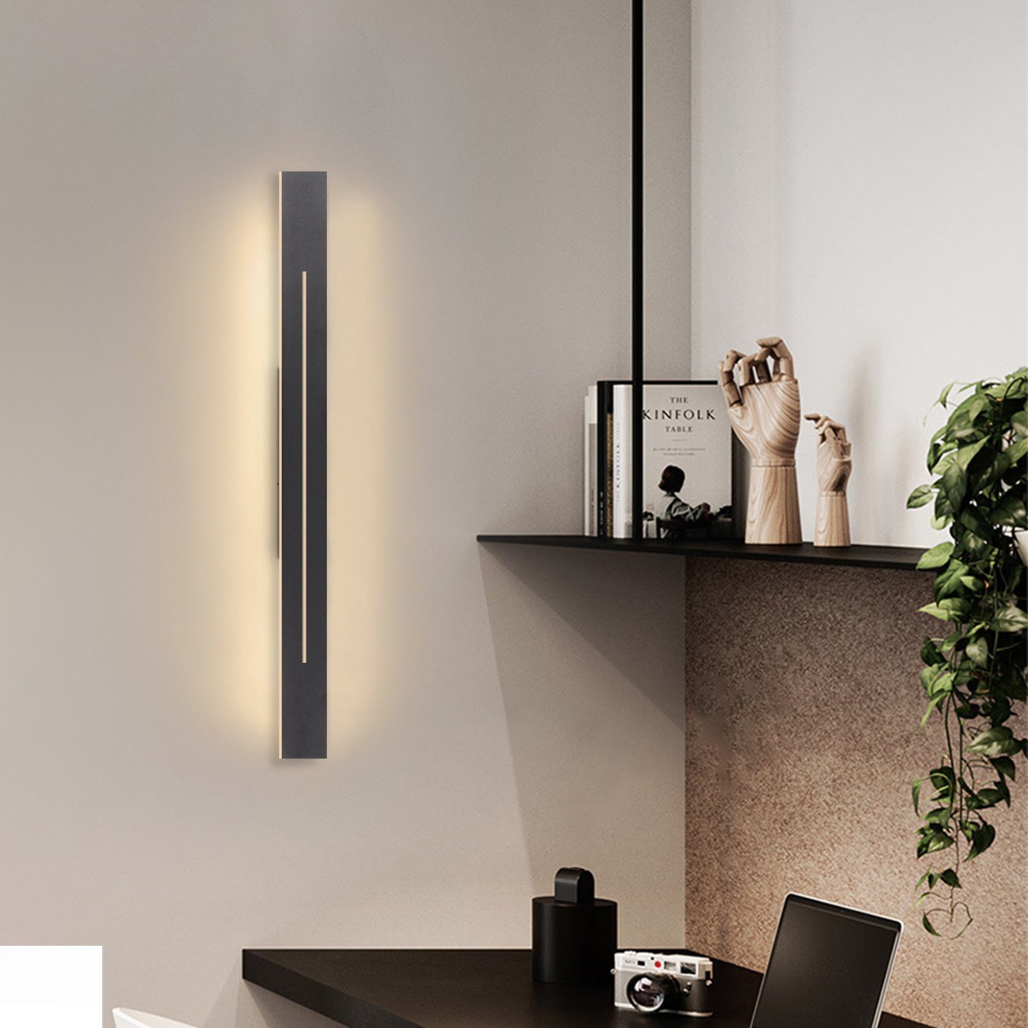 Una lampada da parete nera con luce verticale. Visibile una mensola con decorazioni.