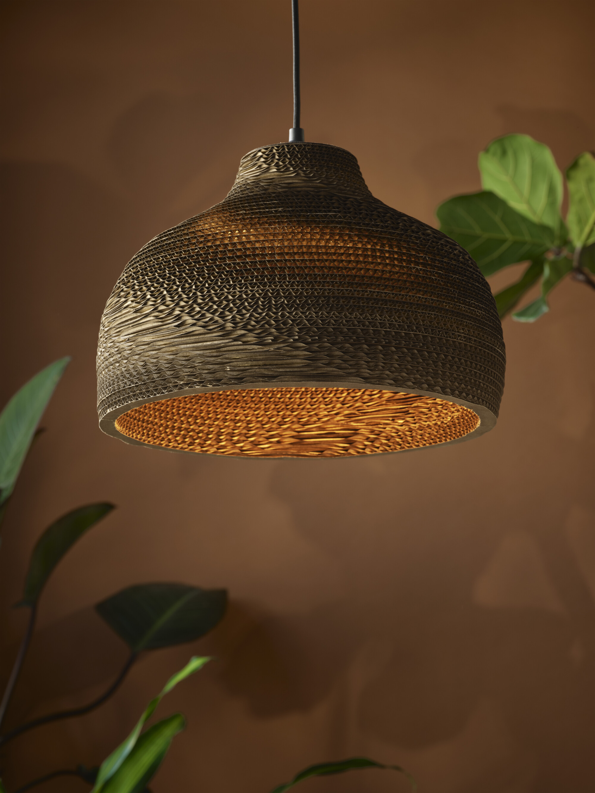 Eine Hängelampe aus geschichtetem braunem Wellpappe, mit warmem Licht.