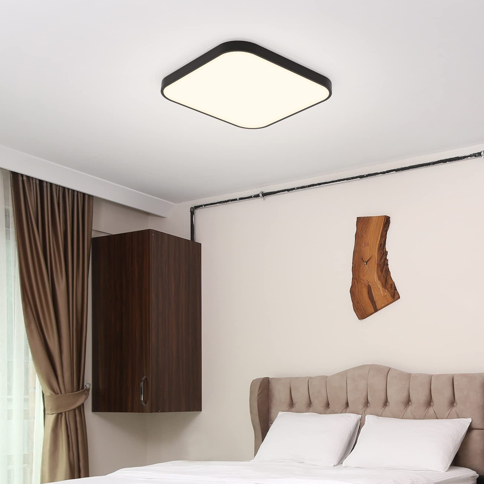 Schlafzimmer mit quadratischer Deckenleuchte, Schrank, Bett mit Kissen und einem Holzkunstwerk an der Wand.