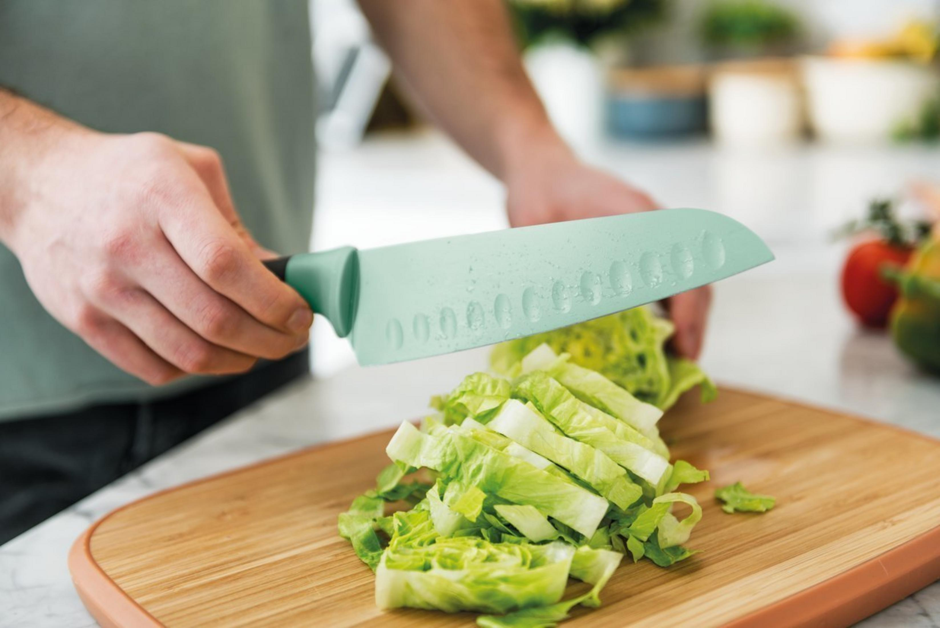 Persoon snijdt sla op een houten snijplank met een groen mes.
