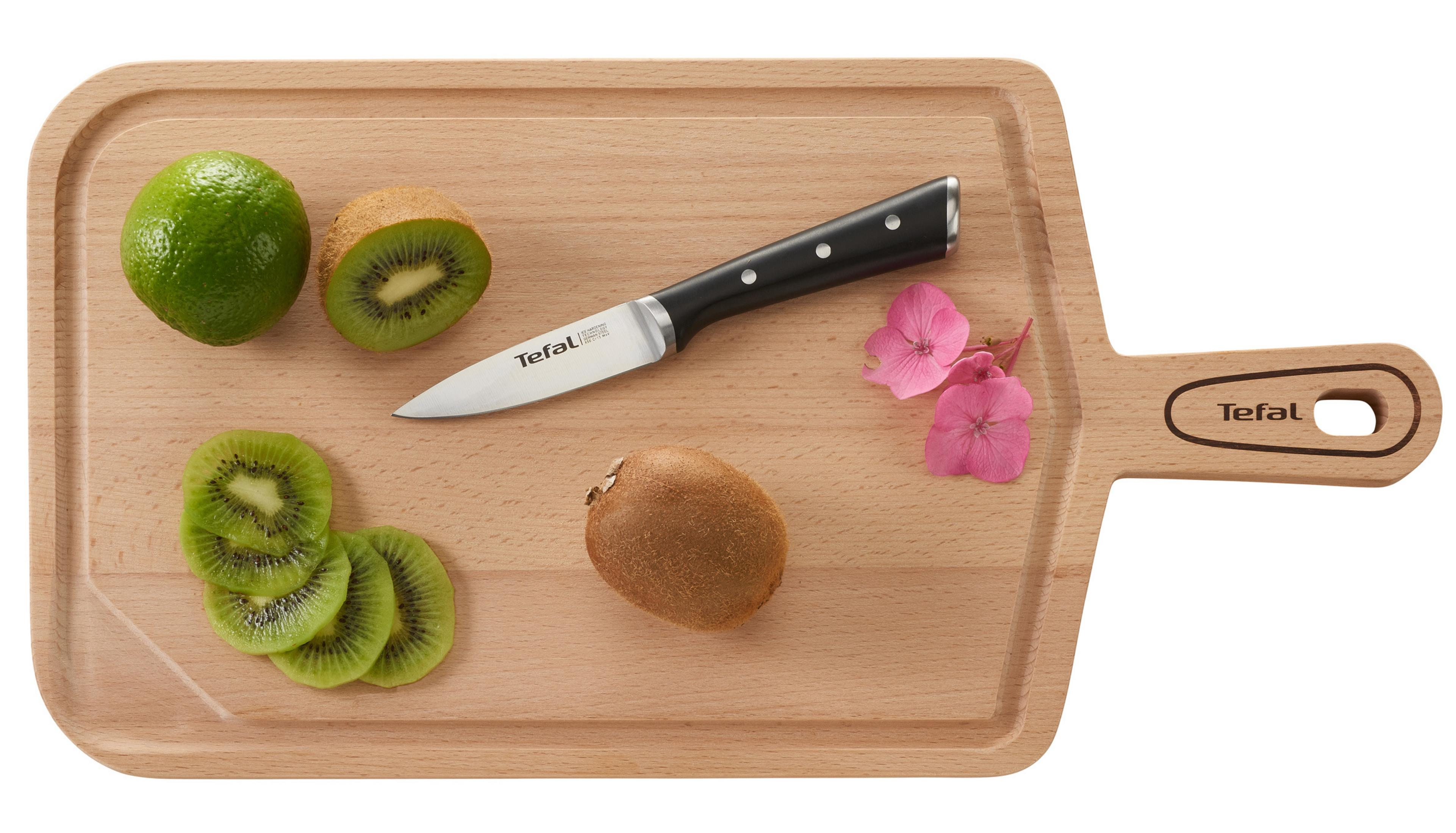 Drewniana deska do krojenia z nożem, plasterkami kiwi, całą kiwi i limonką. Obecne różowe kwiaty.