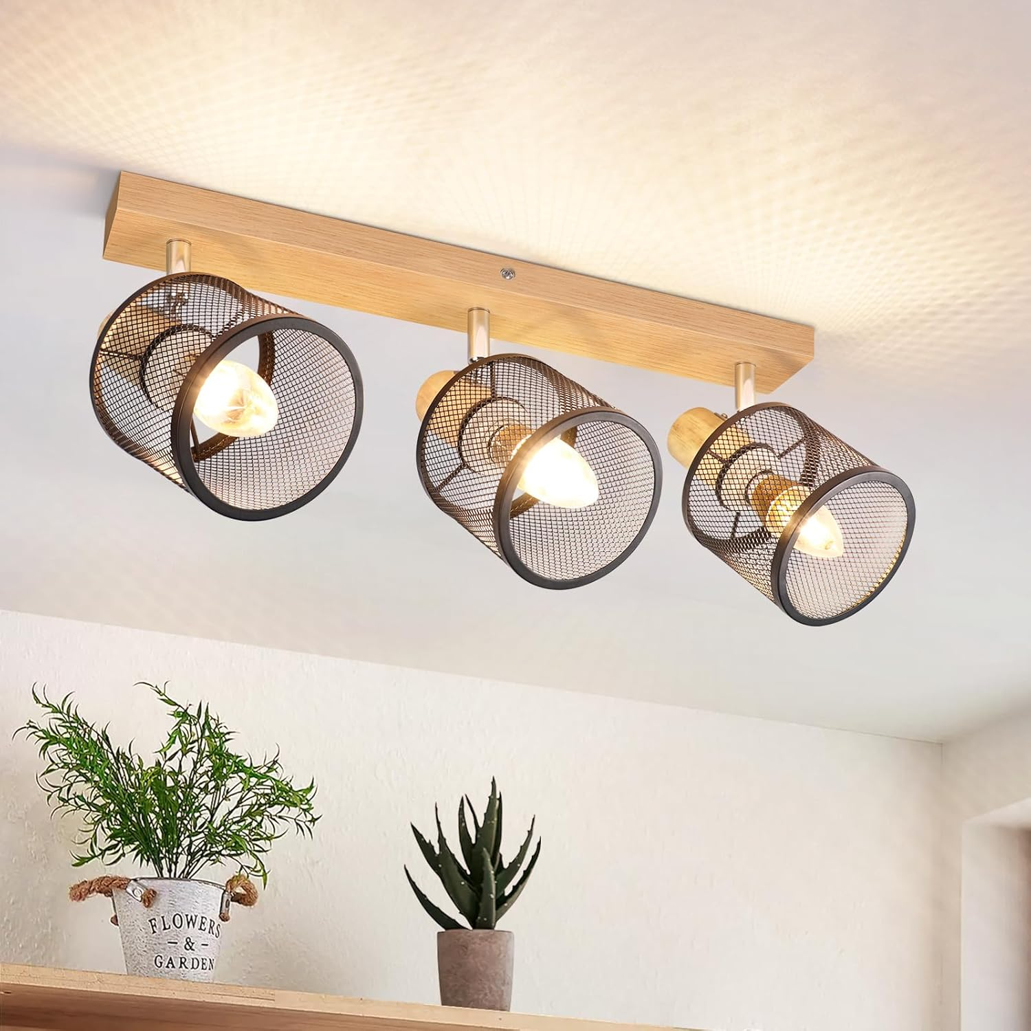 Lampada da soffitto con tre lampade. Trave in legno con paralumi a gabbia metallica. Piante in primo piano.