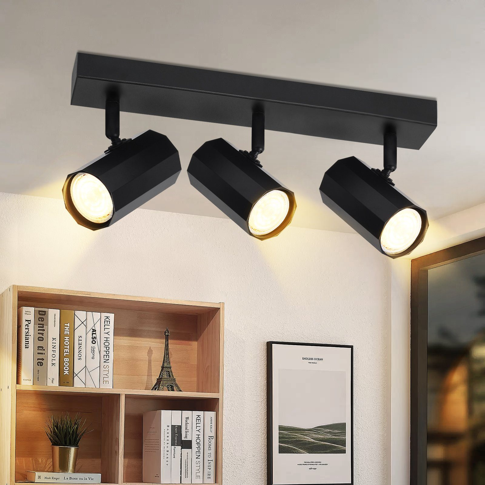 Binario di illuminazione nero con tre faretti orientabili, montati su un soffitto bianco, sopra una libreria e opere d'arte.