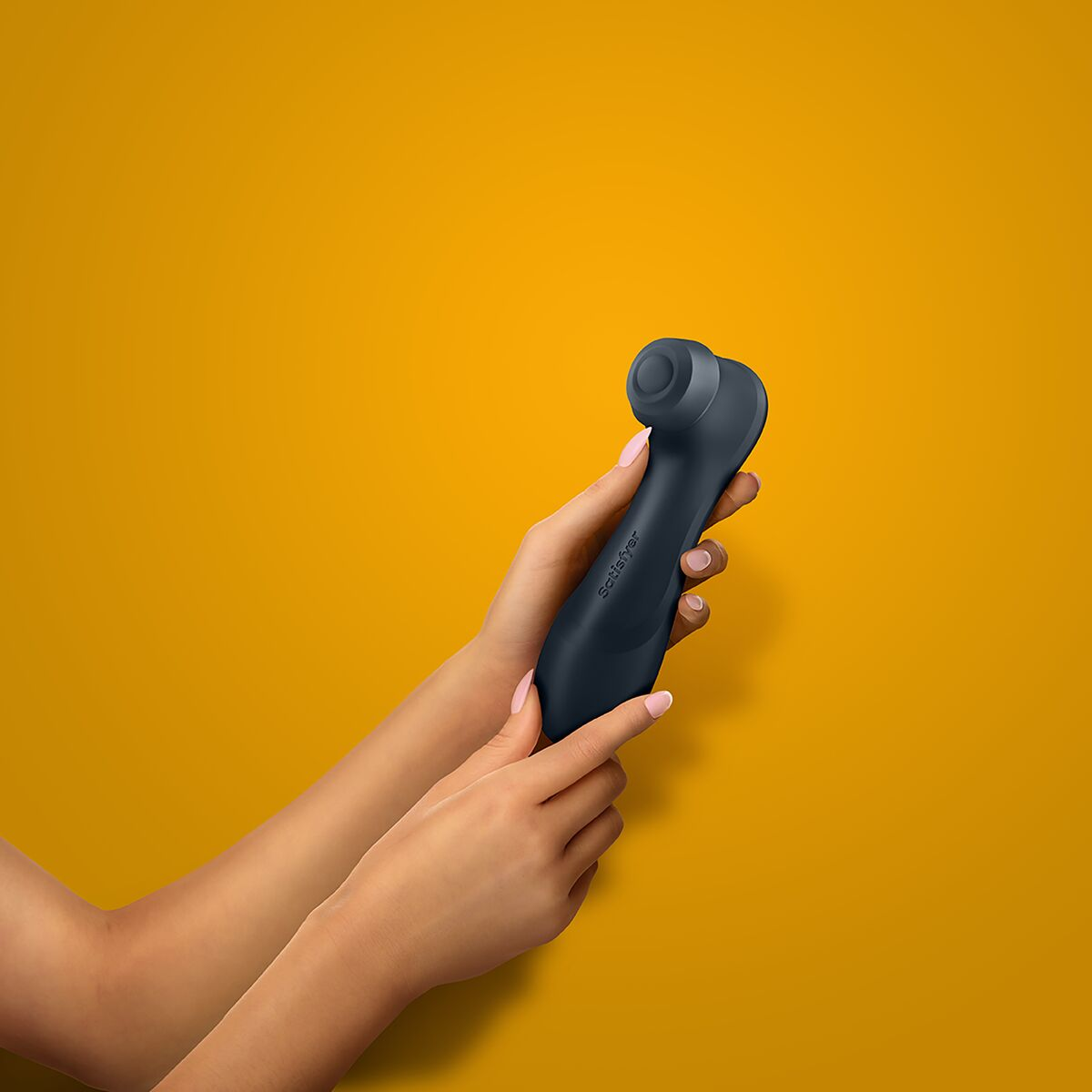 Una persona sosteniendo un vibrador negro contra un fondo naranja, con uñas rosas.