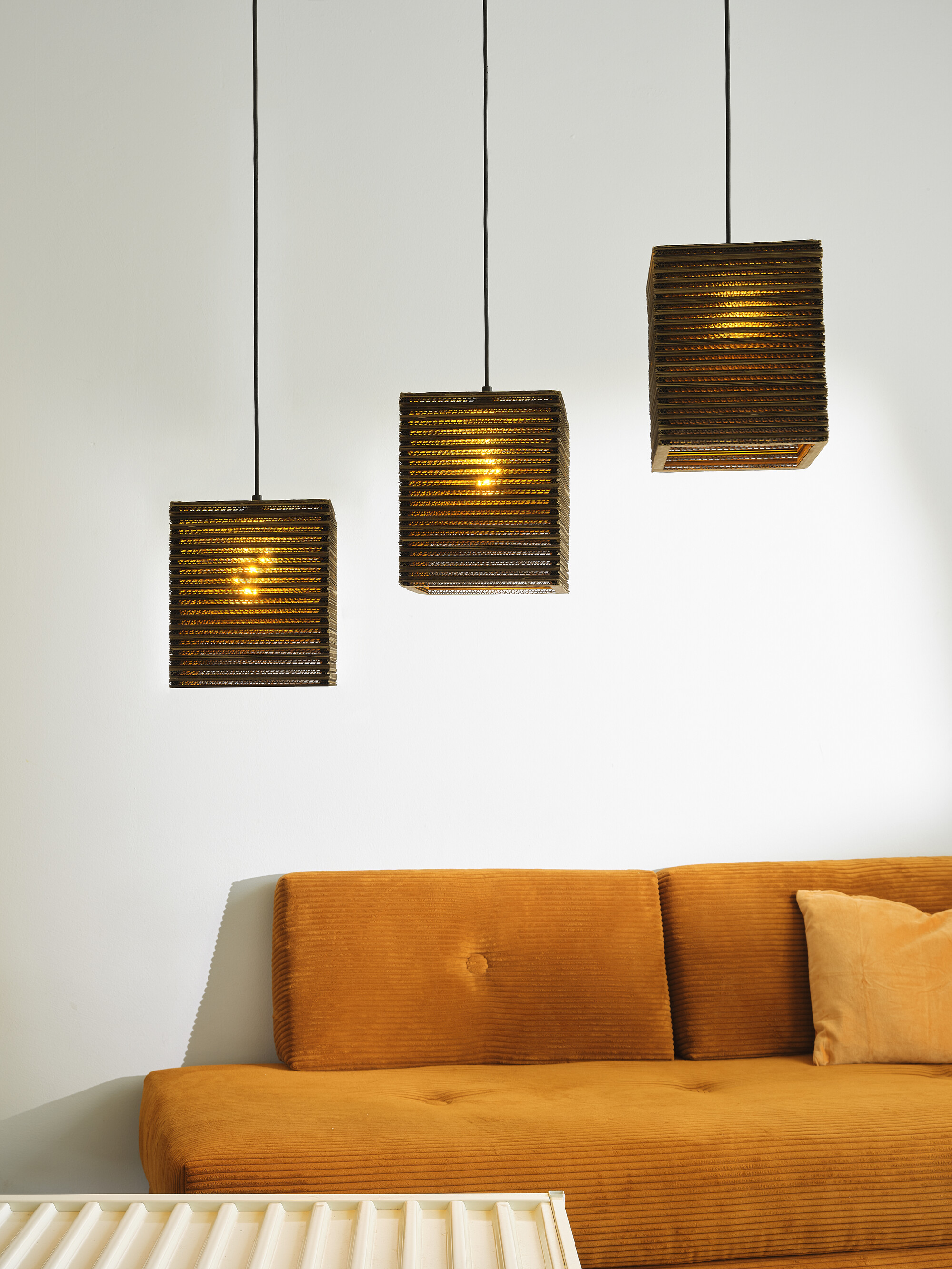 Drei quadratische braune Lampen hängen über einem orangefarbenen Sofa und einem weißen Tisch.