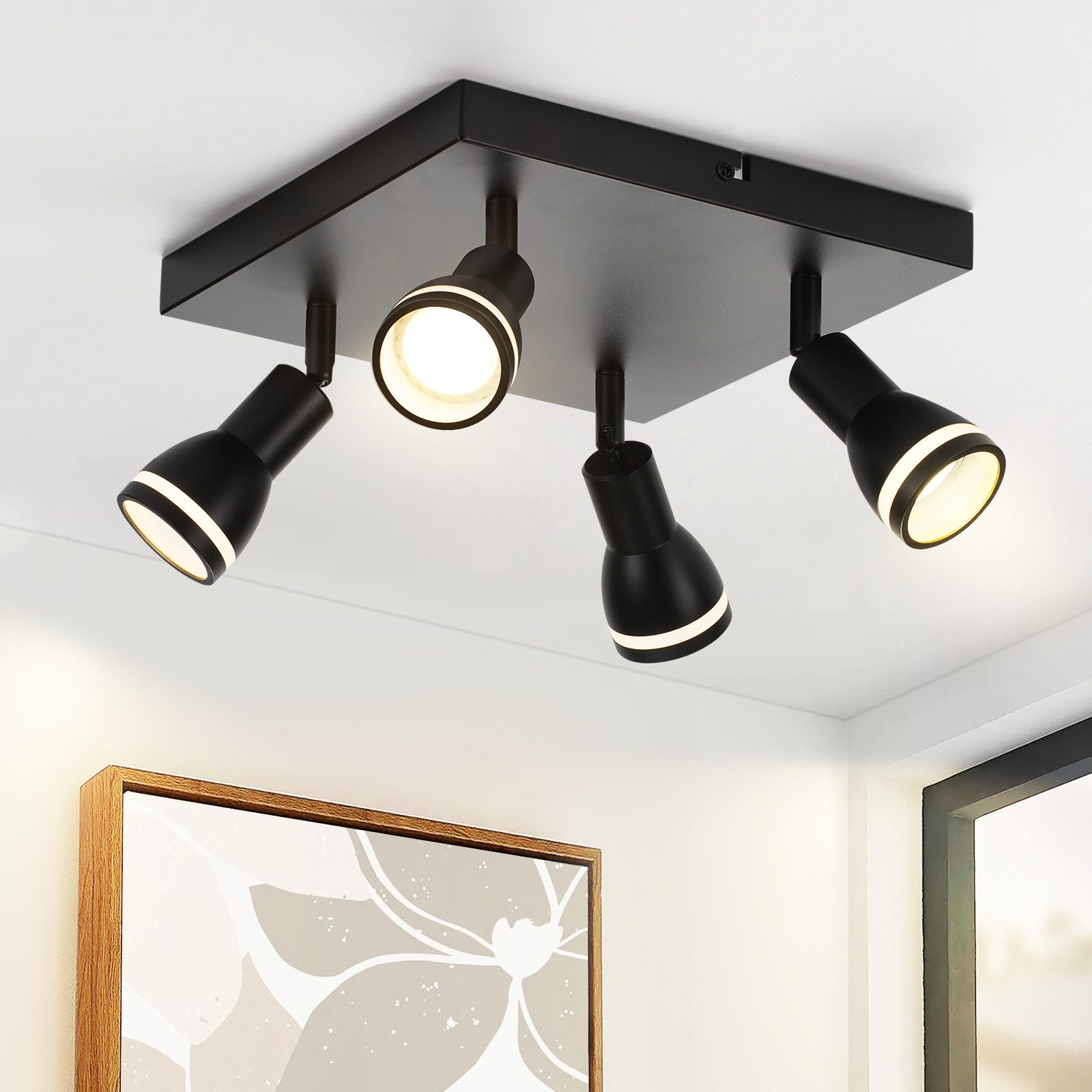 Quattro faretti neri su base quadrata nera, montati su soffitto bianco. Quadro sullo sfondo.
