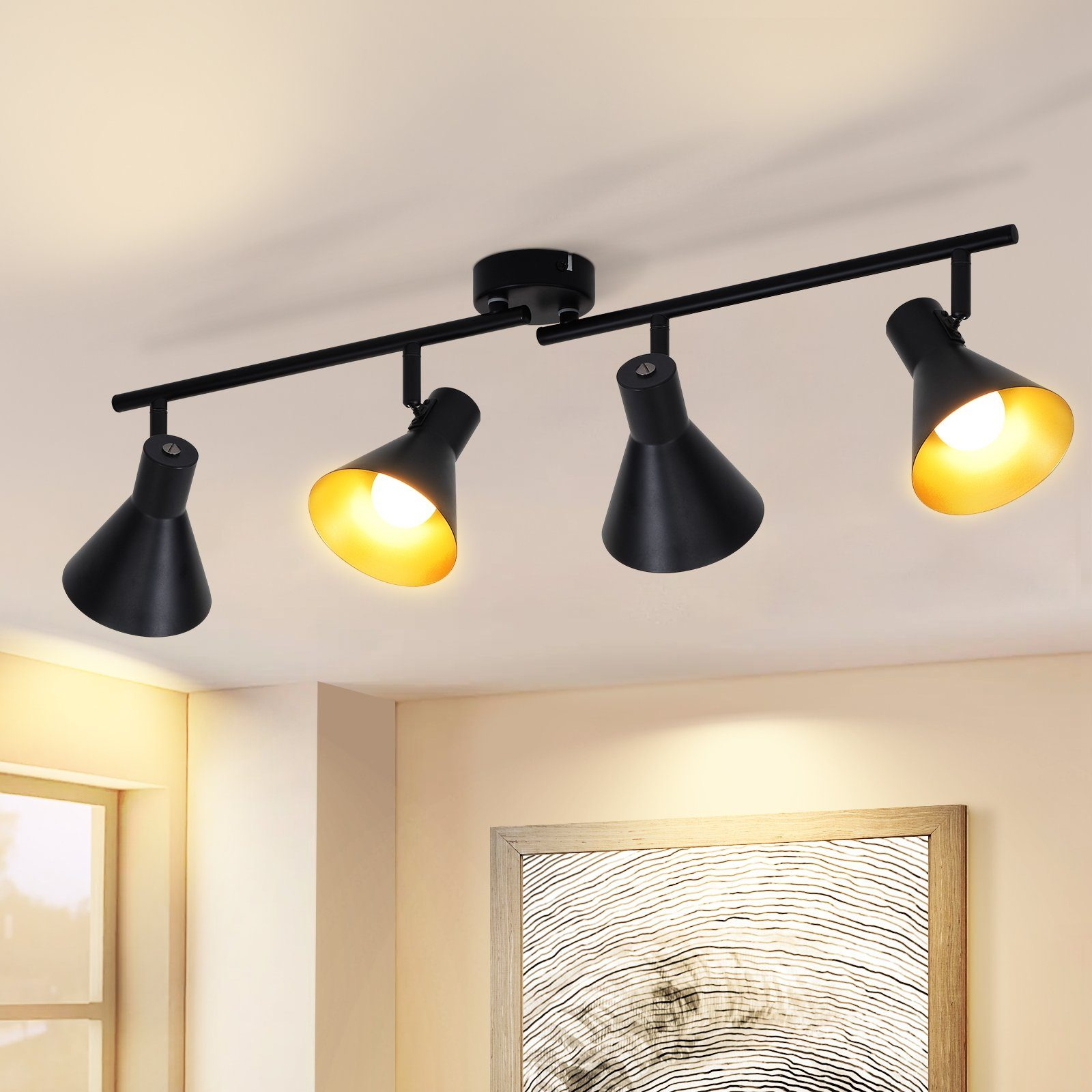 Quattro faretti neri con interni dorati montati su una barra nera su un soffitto beige, illuminati.