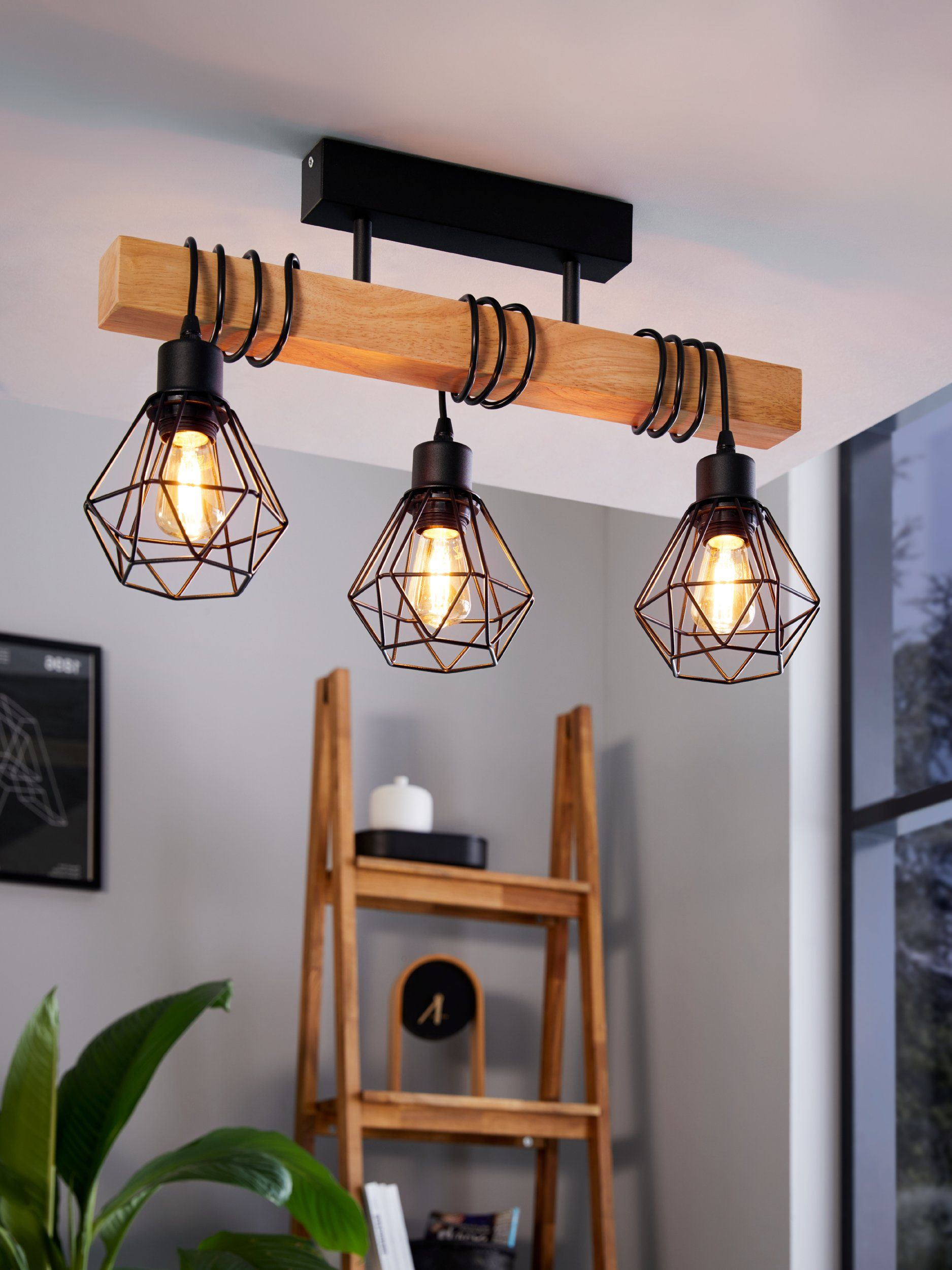 Una trave in legno con tre luci sospese. Le luci hanno telai in metallo nero. Sfondo.