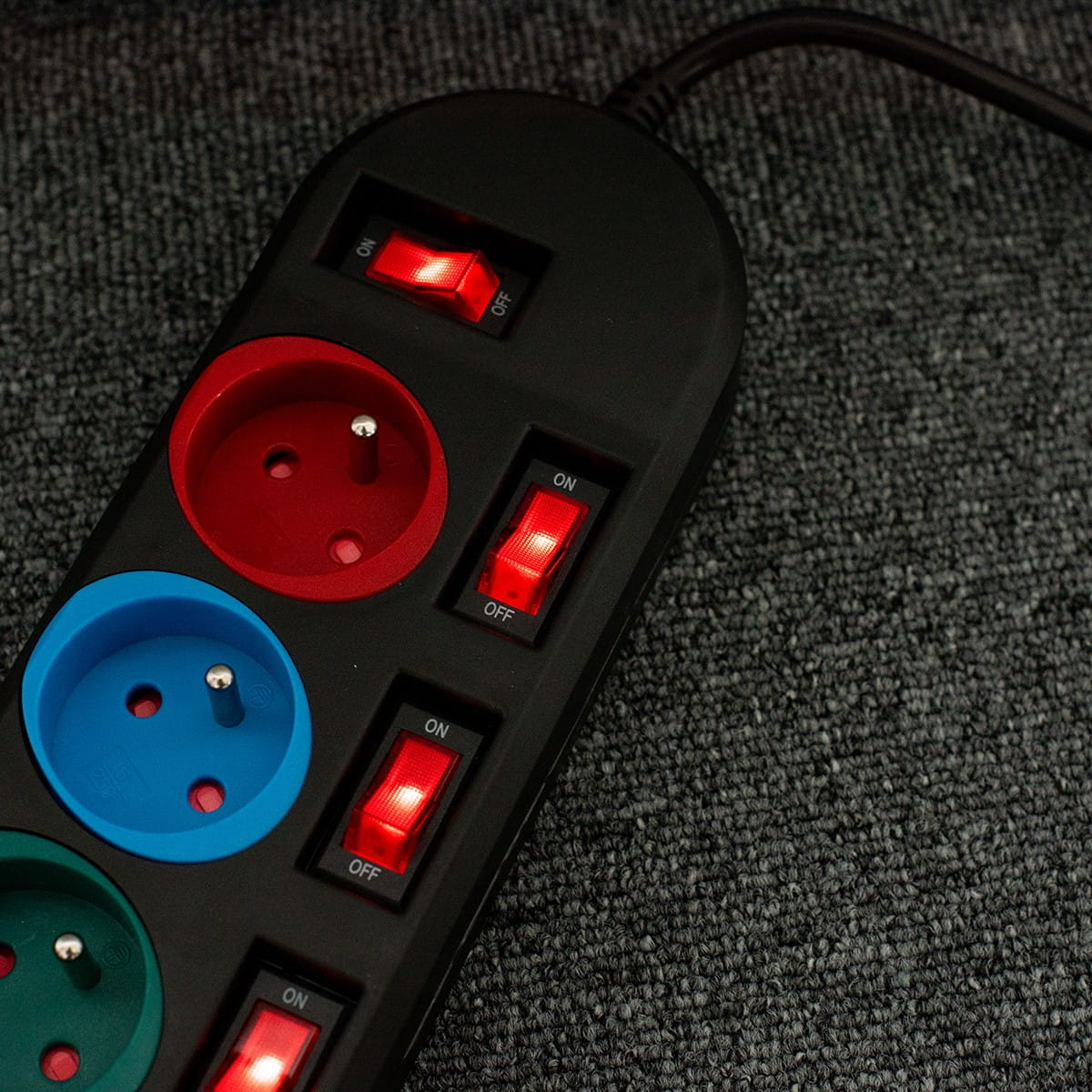 Zbliżenie czarnej listwy zasilającej z kolorowymi gniazdami i przełącznikami.
