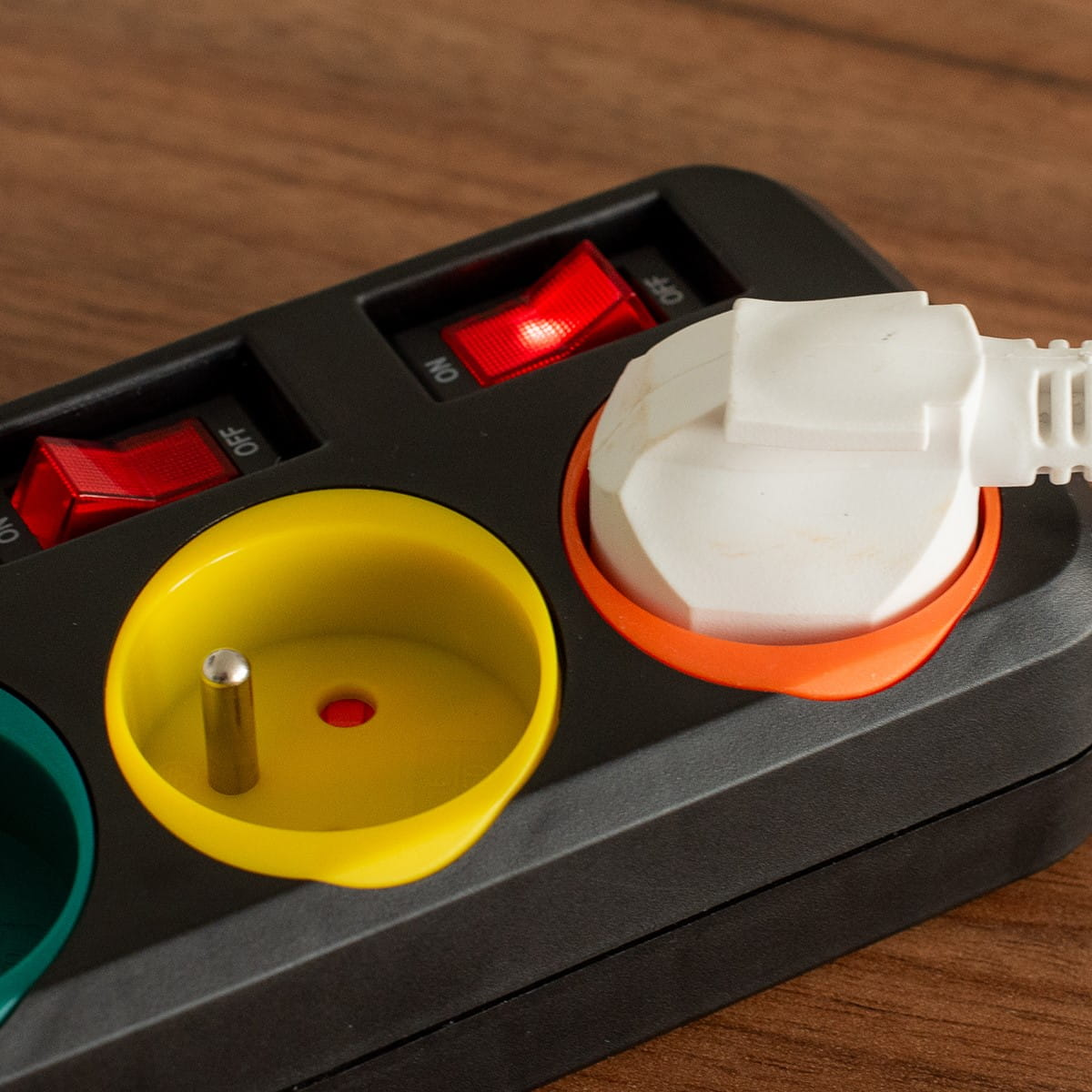 Zbliżenie czarnej listwy zasilającej z włożoną białą wtyczką i podświetlonym czerwonym przełącznikiem.