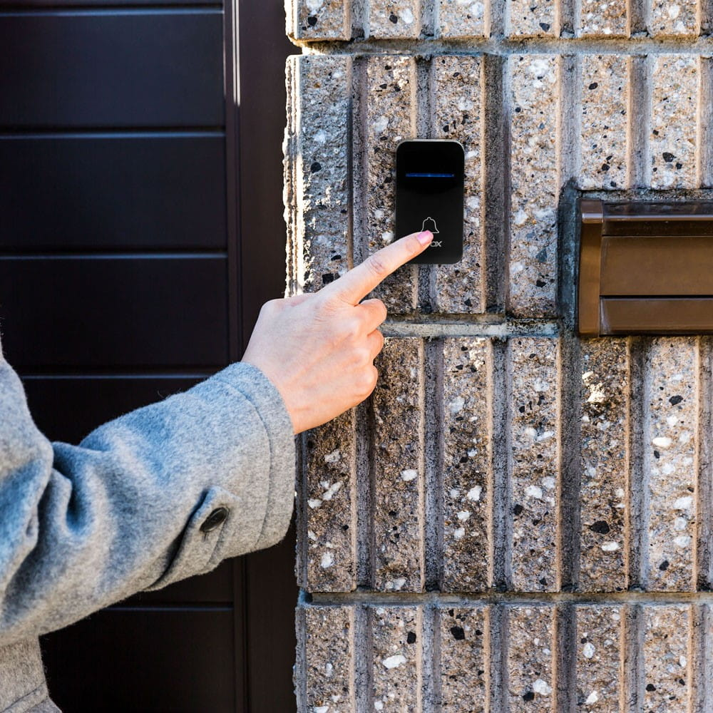 Palec naciska czarny dzwonek do drzwi na ceglanej ścianie.