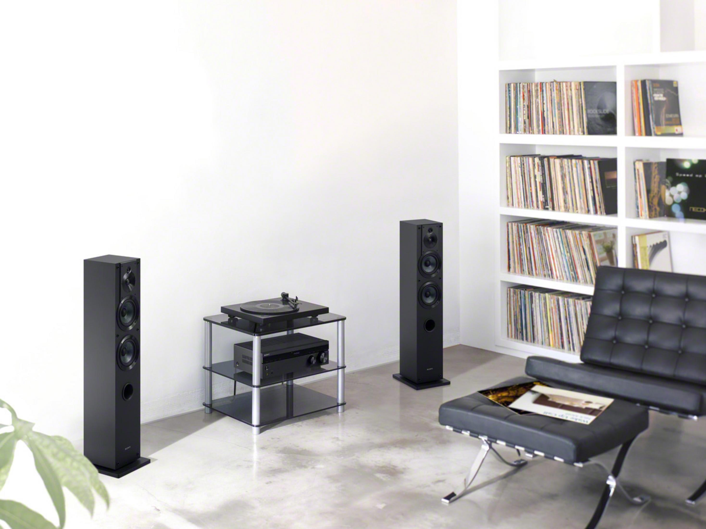 Salón con dos altavoces, una mesa de cristal con tocadiscos y una estantería.