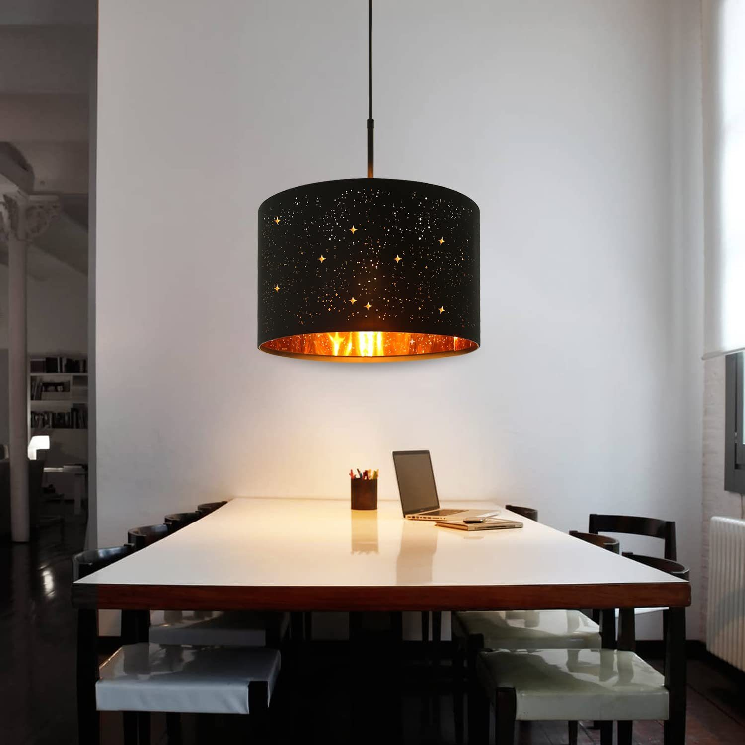 Schwarze Pendelleuchte mit Sternaussparungen, über einem weißen Tisch im Raum.