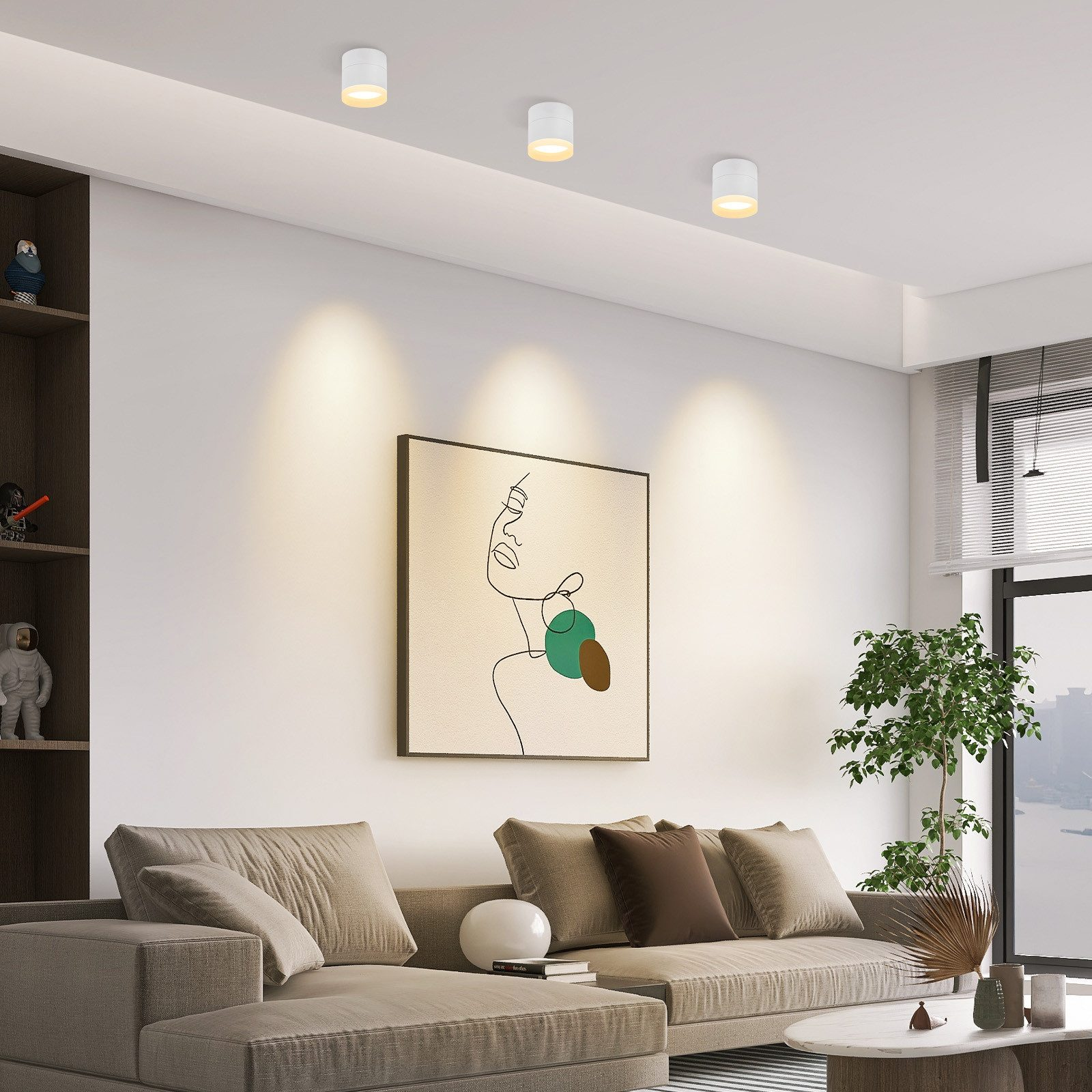 Soggiorno con divano beige, opere d'arte e faretti a incasso. Pareti bianche e una grande finestra sullo sfondo.