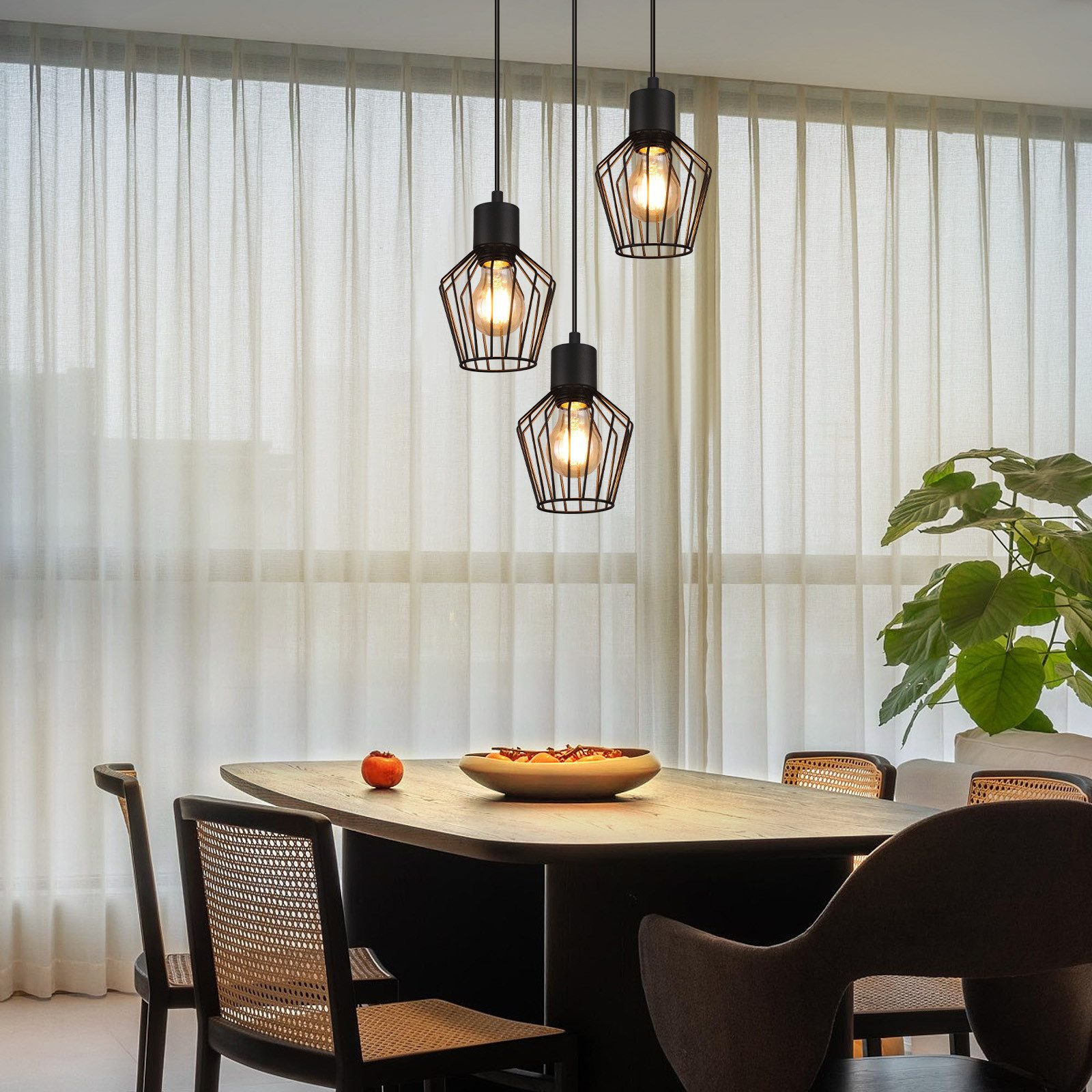 Drei schwarze Pendelleuchten mit Edison-Glühbirnen über einem Esstisch mit Stühlen.
