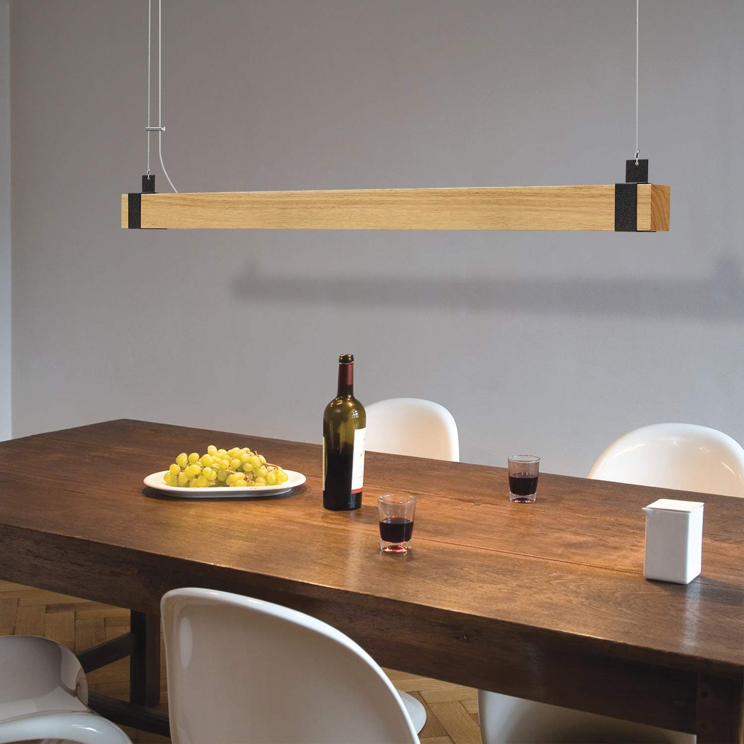 Ein Holztisch mit Weinflasche, Trauben und Gläsern. Eine Leuchte hängt darüber.