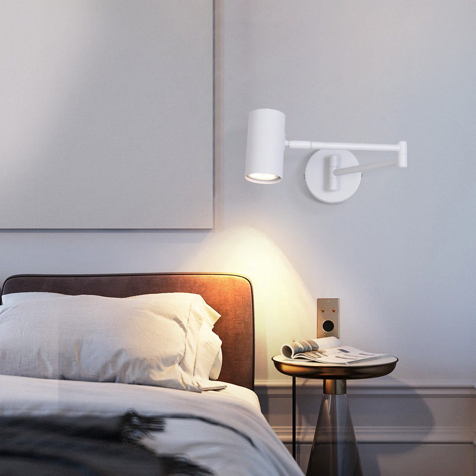 Una lampada da parete bianca regolabile illumina un letto, un comodino e un'opera d'arte in una stanza.