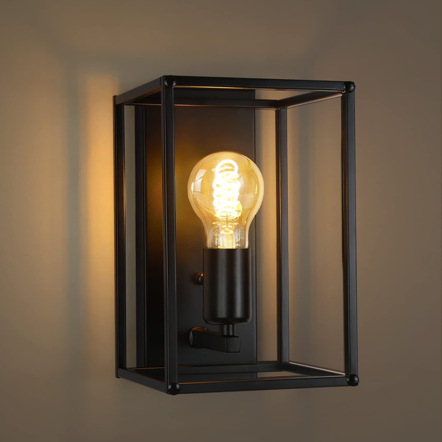 Primo piano di una lampada da parete nera, in gabbia, con una lampadina a spirale accesa.