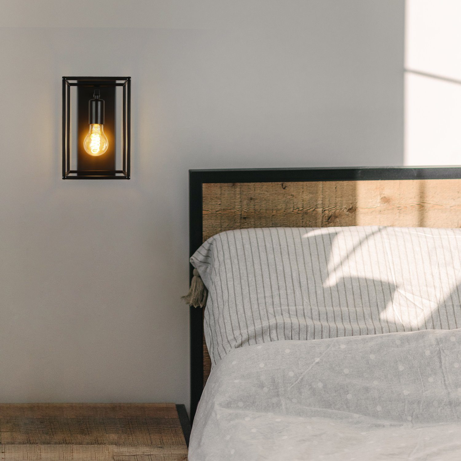Una lampada da parete nera con lampadina visibile accanto a un letto.