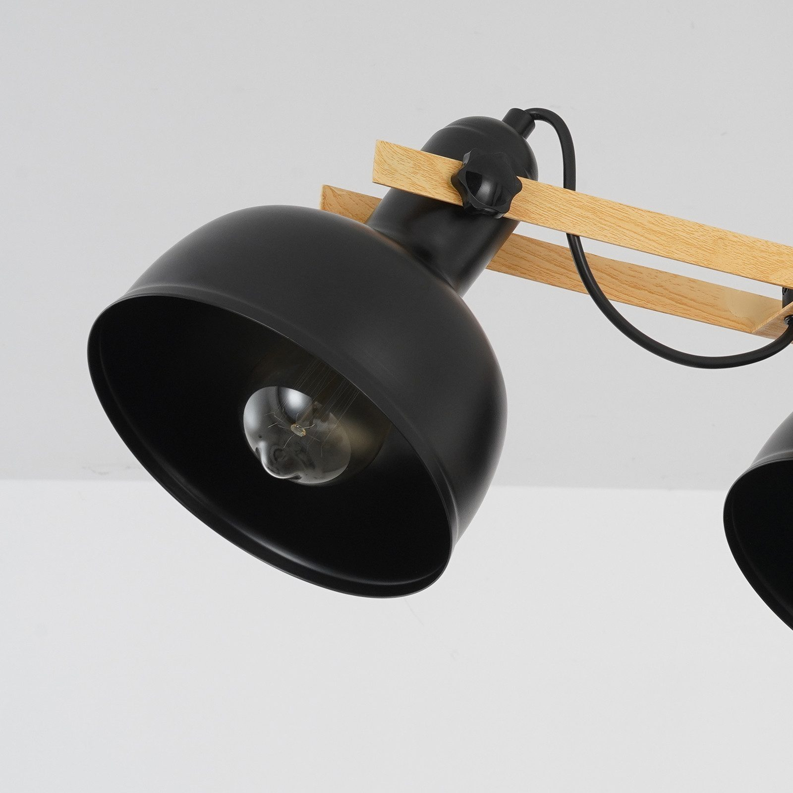 Zbliżenie czarnej lampy wiszącej z drewnianą belką i widoczną żarówką.