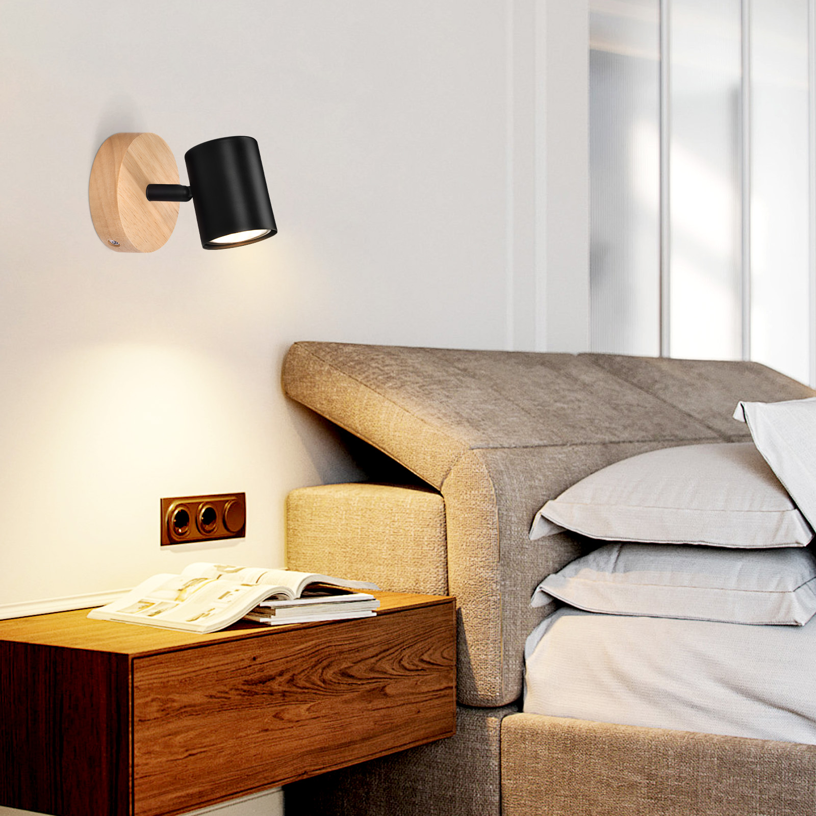 Faretto nero a parete su base in legno, che illumina un libro e un letto in una camera da letto.