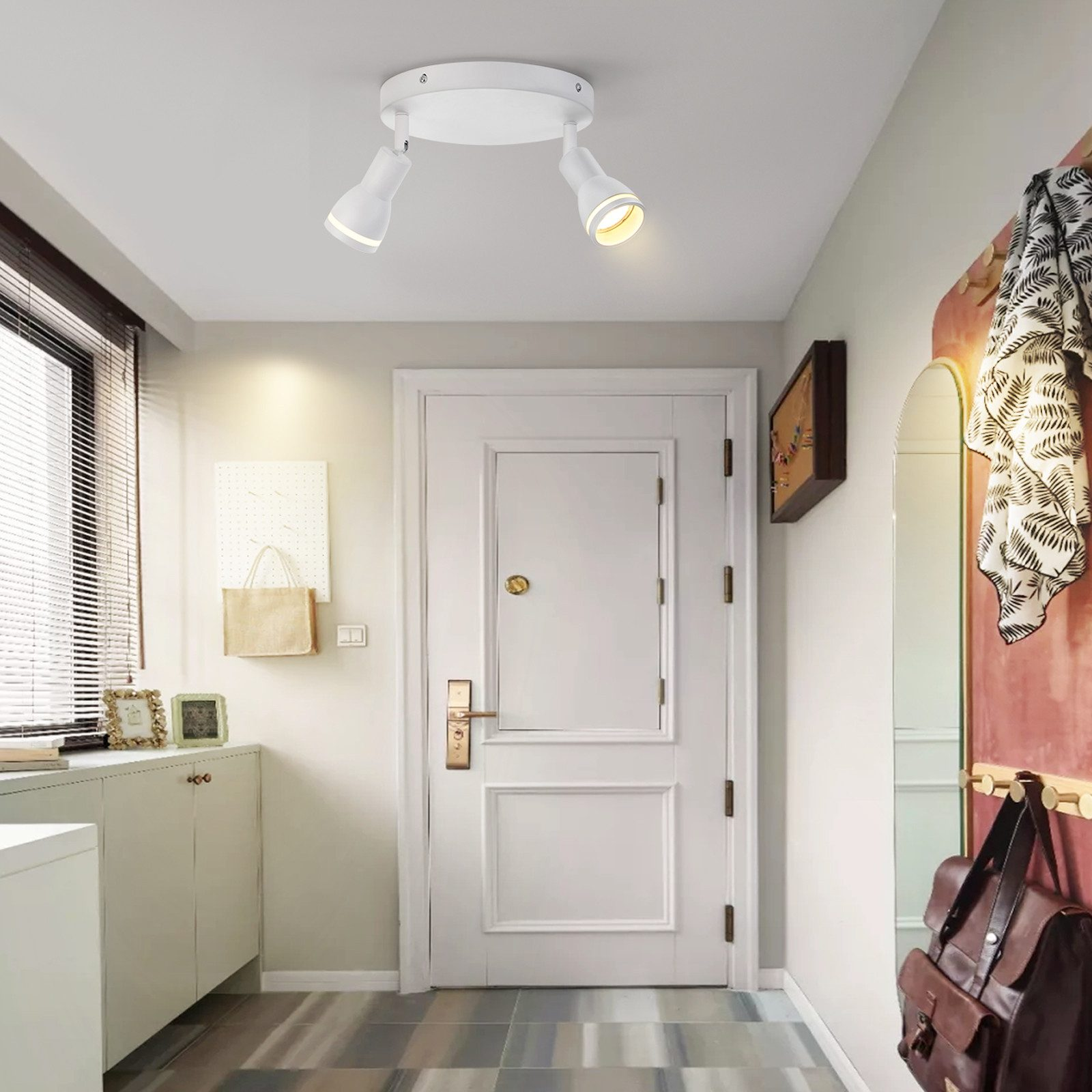 Due faretti bianchi su un soffitto bianco, che illuminano un corridoio con una porta e decorazioni.