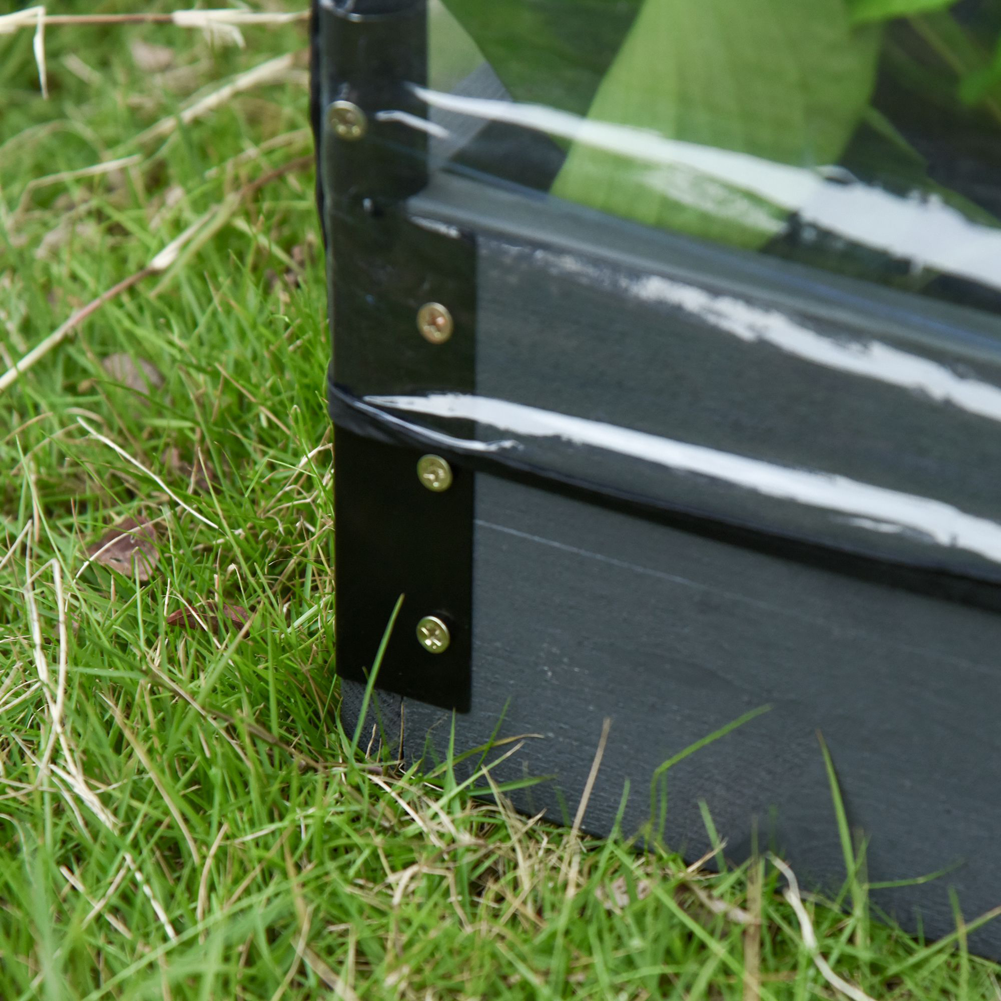 Nahaufnahme einer Gartenecke. Schwarze Eckstücke mit Schrauben auf grünem Gras.