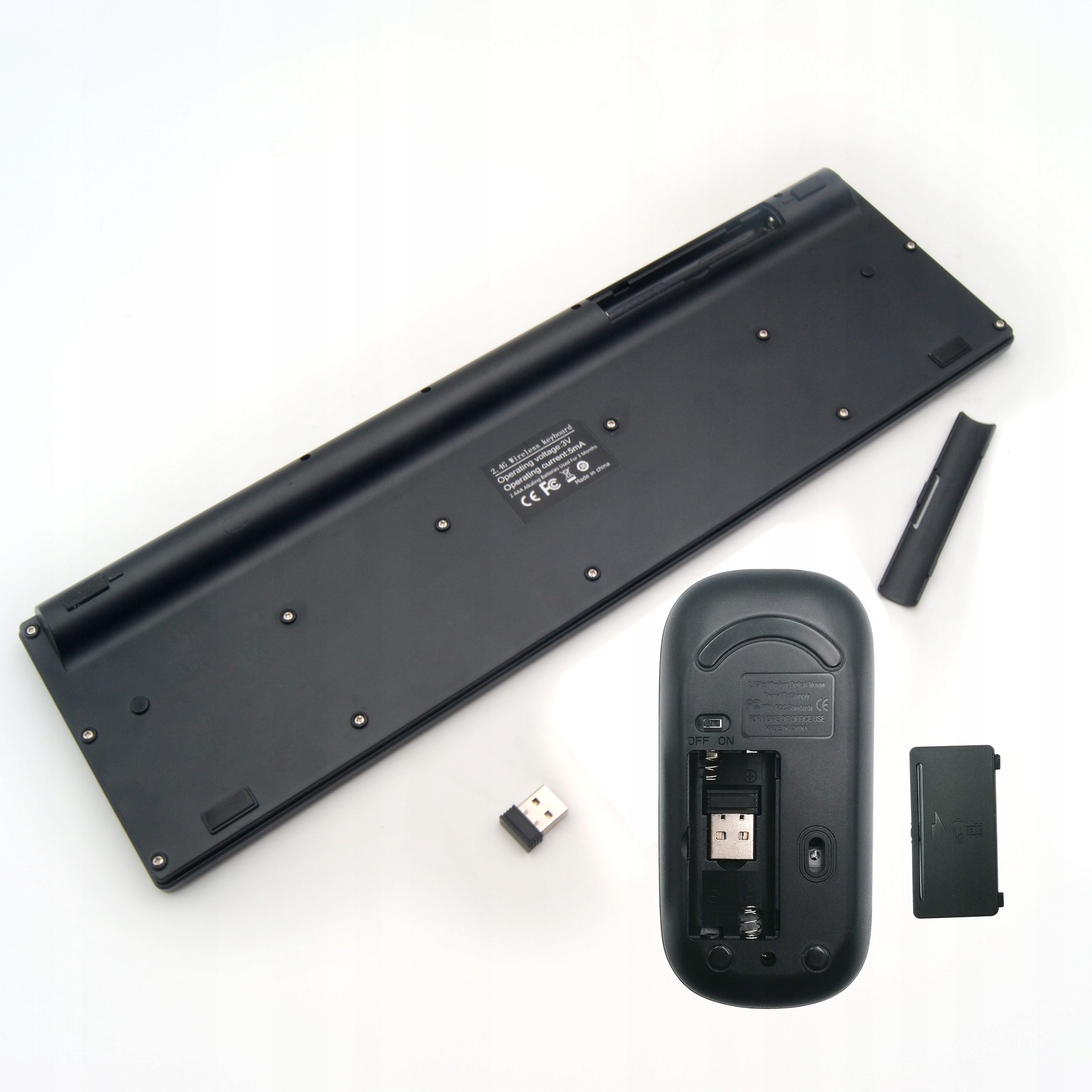 Spód klawiatury i myszy, z przegródkami na baterie i odbiornikiem, na białym tle.