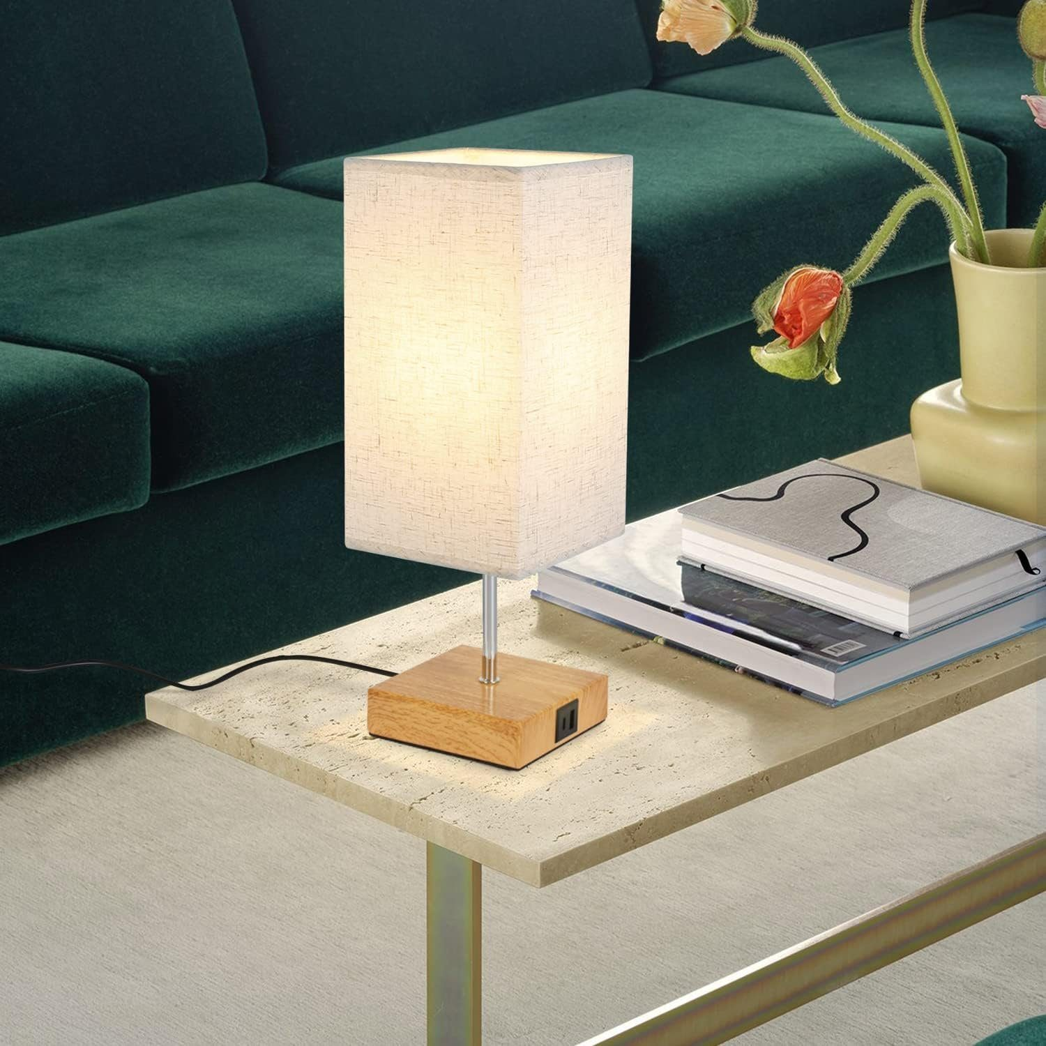 Lampa na stole z książkami i kwiatami. Zielona sofa w tle. Otoczenie jest przytulne.