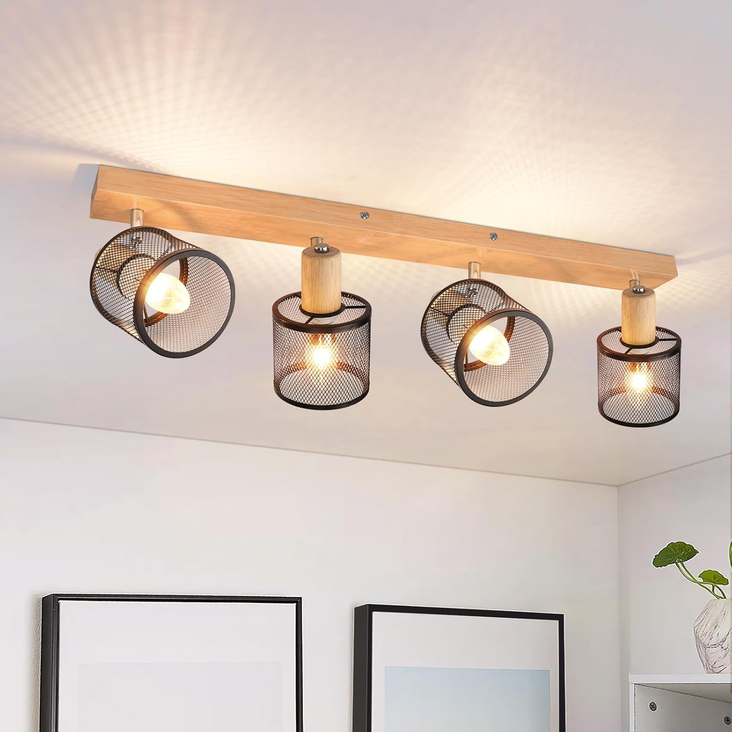 Quattro faretti su una trave di legno, con soffitto bianco e due quadri incorniciati.