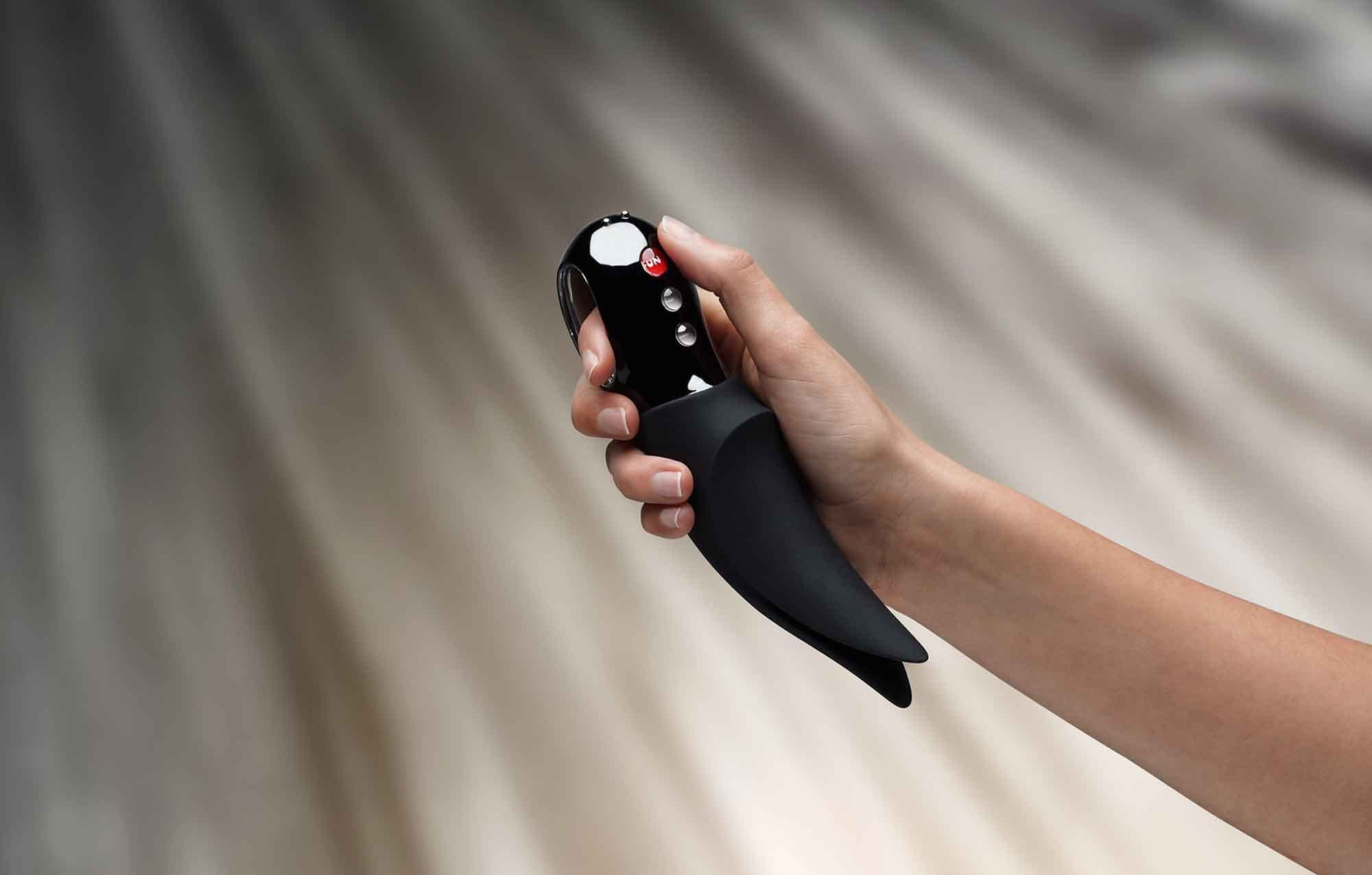 Czarna zabawka erotyczna trzymana w dłoni. Zabawka ma przyciski i zakrzywiony kształt.