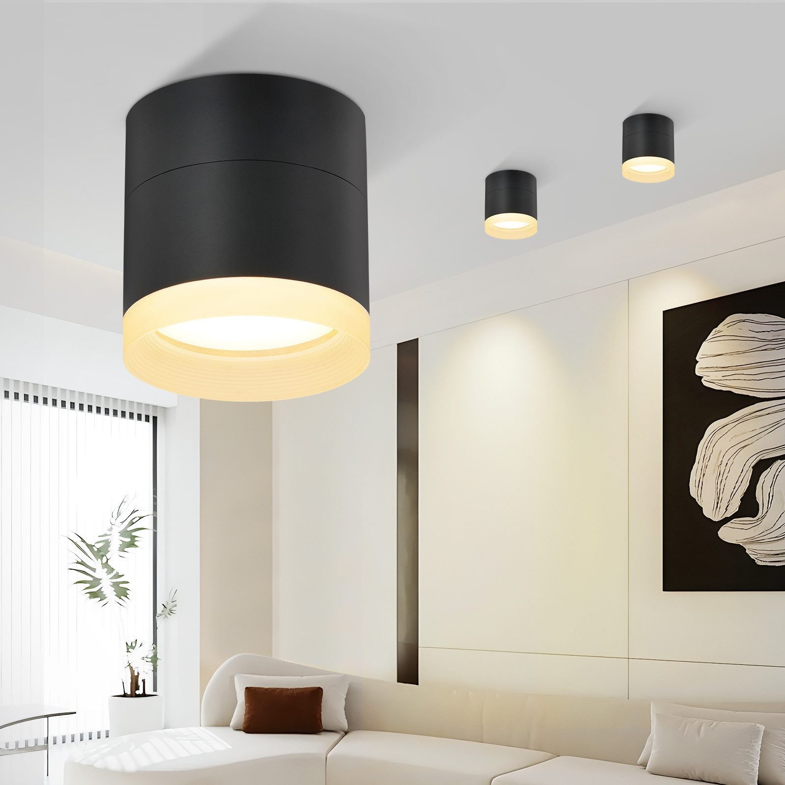 Tre lampade da soffitto nere con illuminazione bianca e gialla. Parete bianca e divano bianco sullo sfondo.