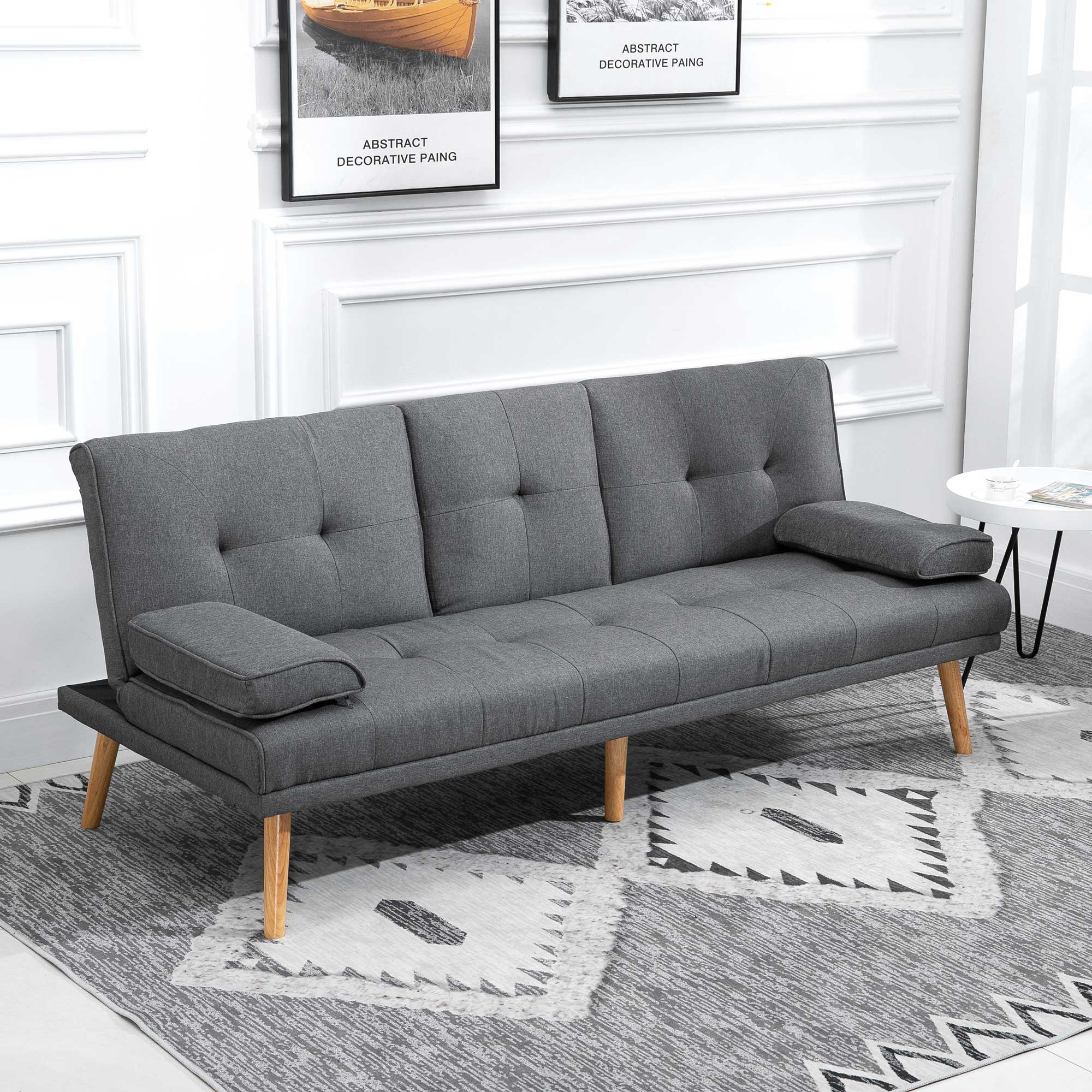 Graues Sofa mit Holzbeinen, zwei Armlehnen, auf einem gemusterten Teppich, zwei Bilder an der Wand.