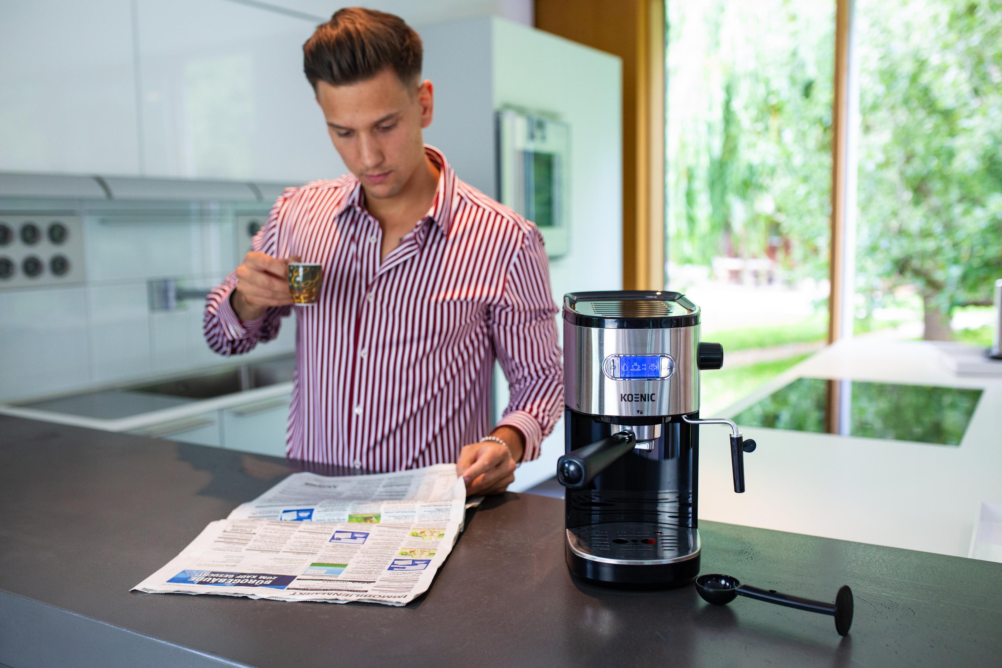 Un hombre bebe café, lee un periódico cerca de una cafetera. La escena tiene lugar en una cocina.