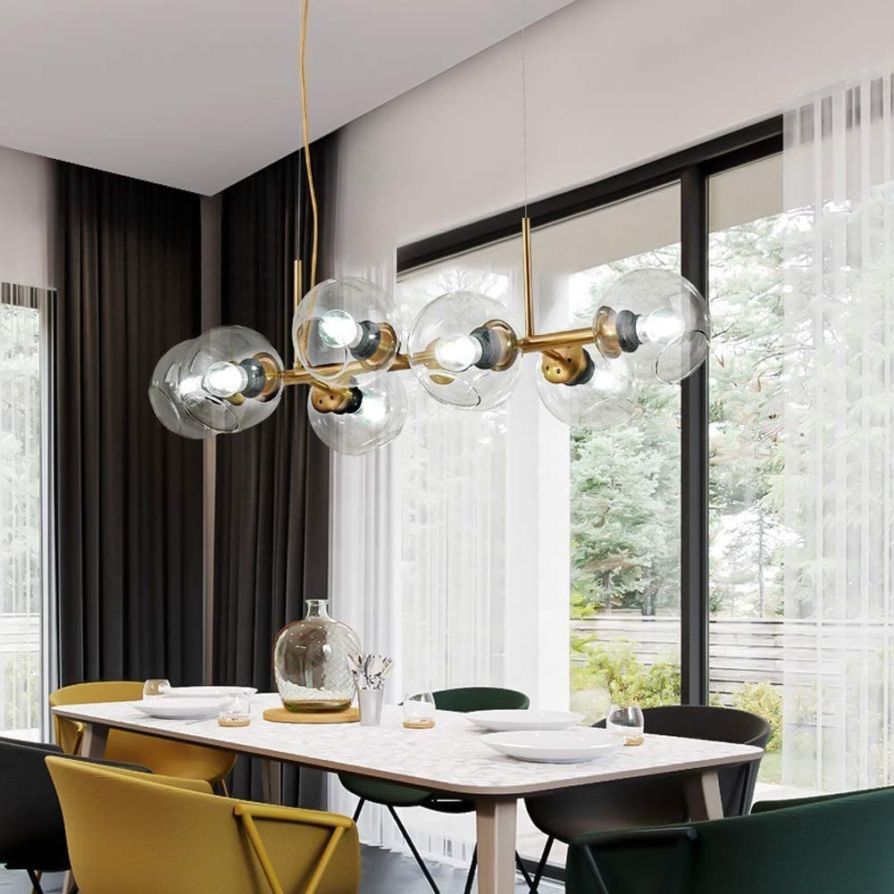 Ein Esszimmer mit Tisch und Kronleuchter. Große Fenster im Hintergrund zeigen eine Außenansicht.