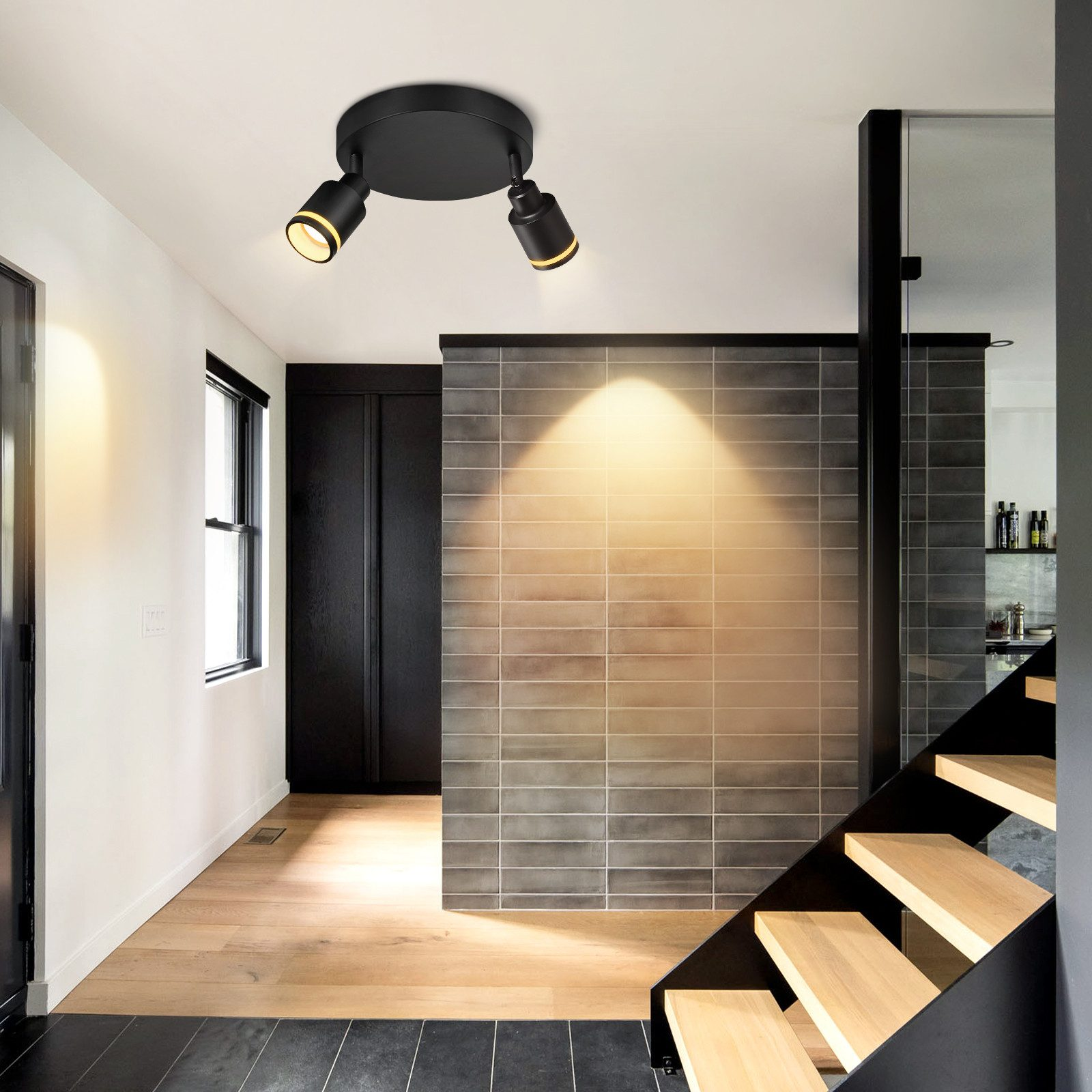 Due faretti neri su una base nera a soffitto. Le luci sono in un corridoio con scale e pavimenti in legno.
