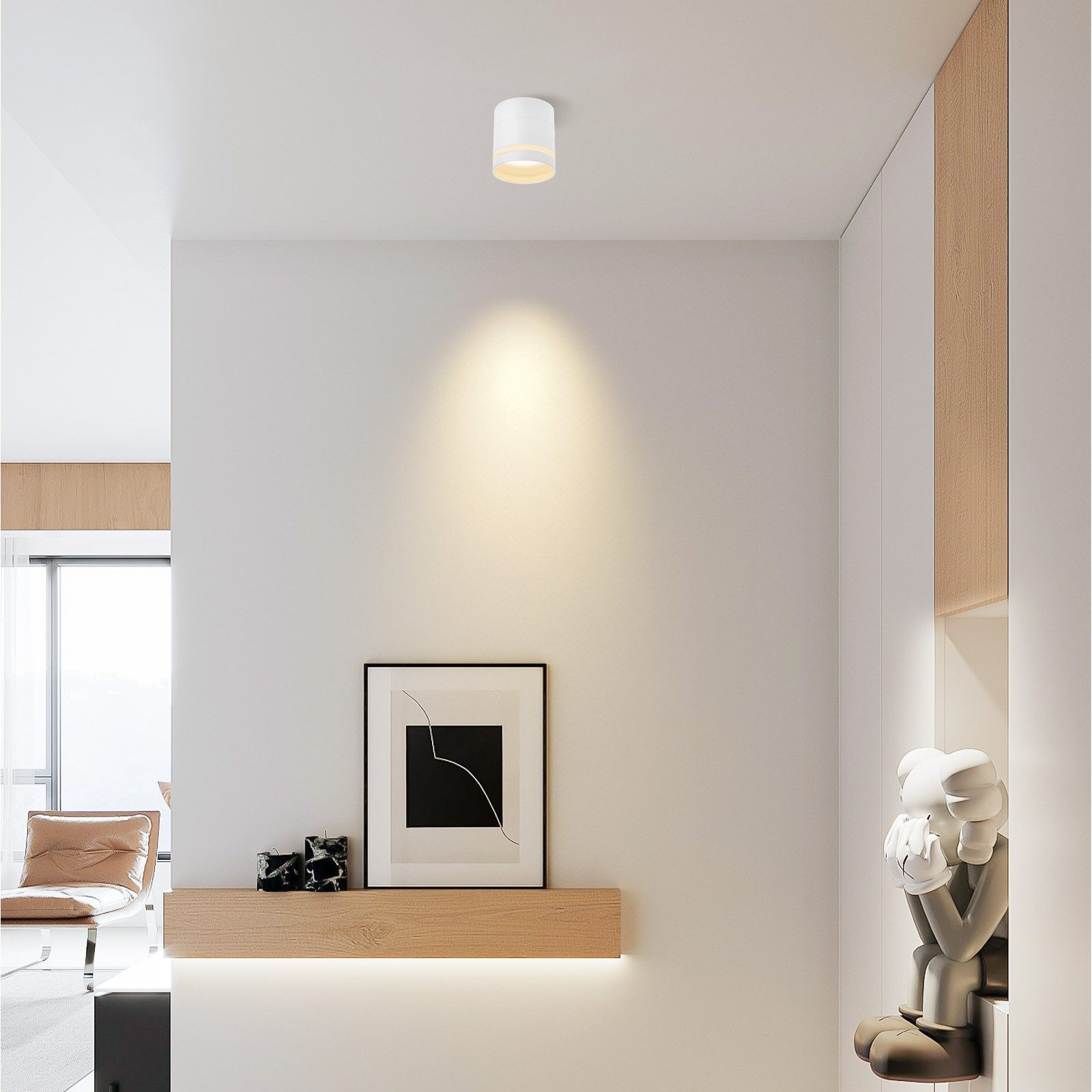 Interno con una luce a soffitto bianca. Un'opera d'arte incorniciata e una statua sono su una mensola di legno contro un muro bianco.