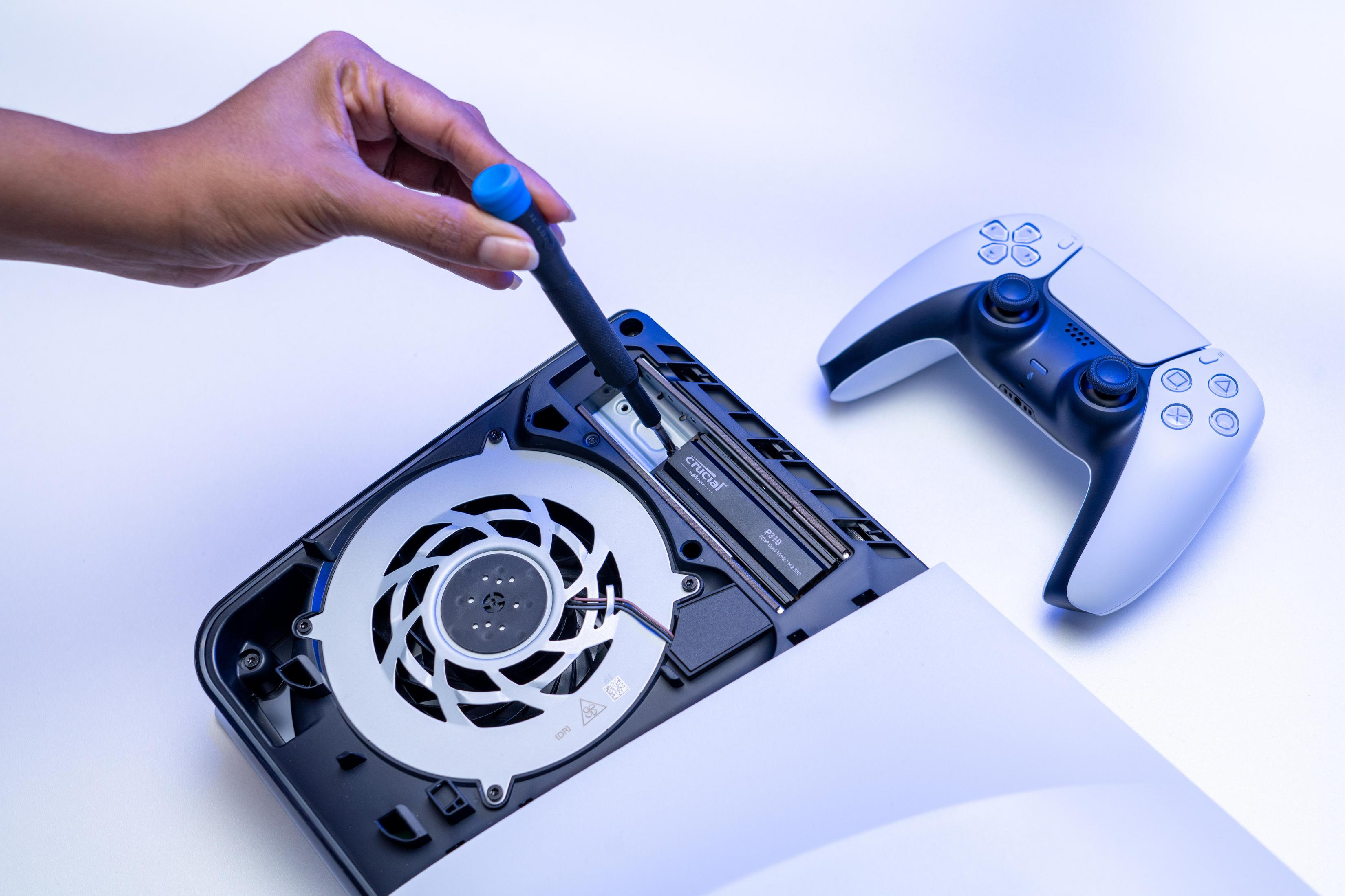 Osoba używająca śrubokręta na PS5. Obok biały kontroler.