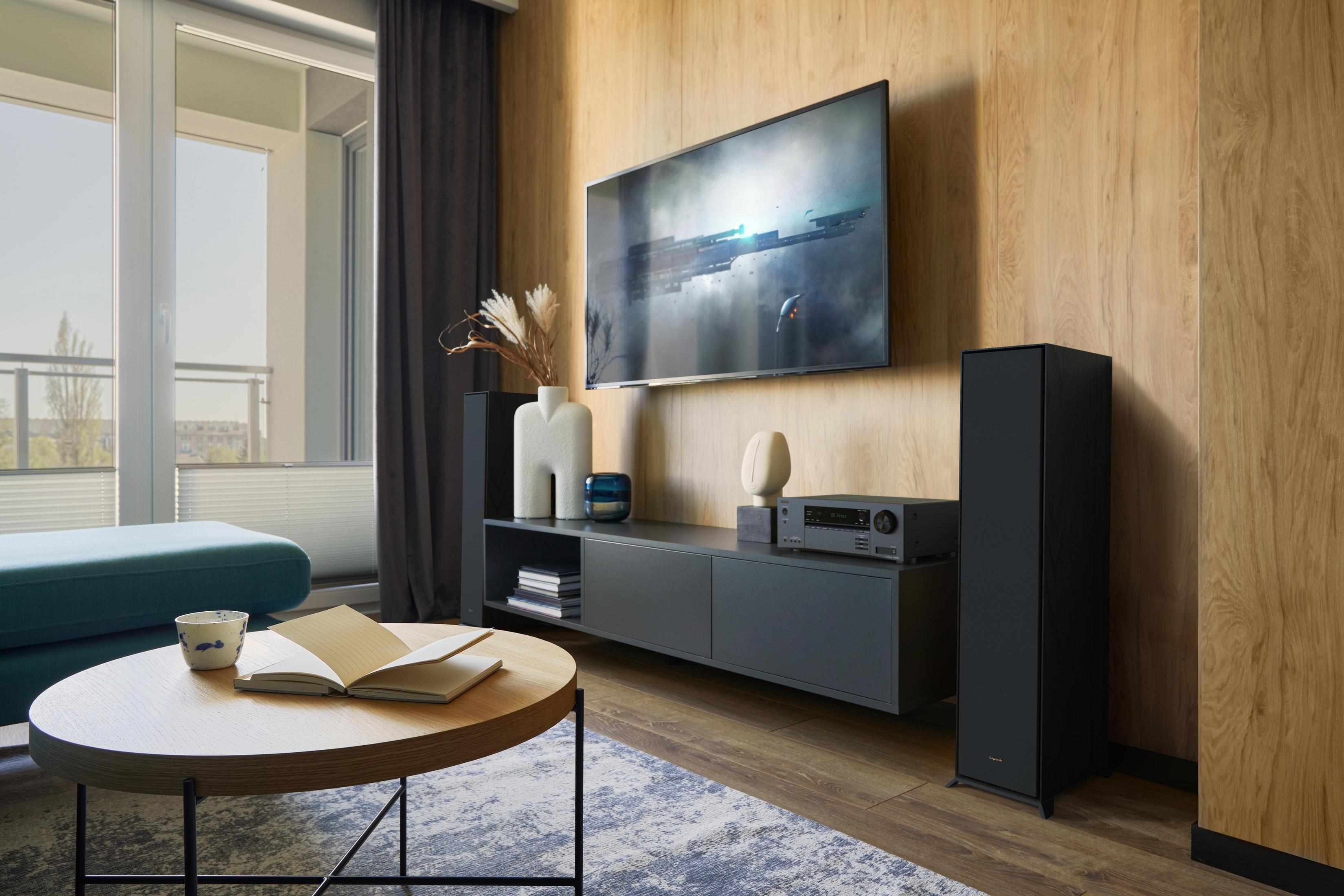 Ein Wohnzimmer mit einem Fernseher an der Wand, einem Sofa, einem Couchtisch mit einem Buch und dekorativen Elementen.