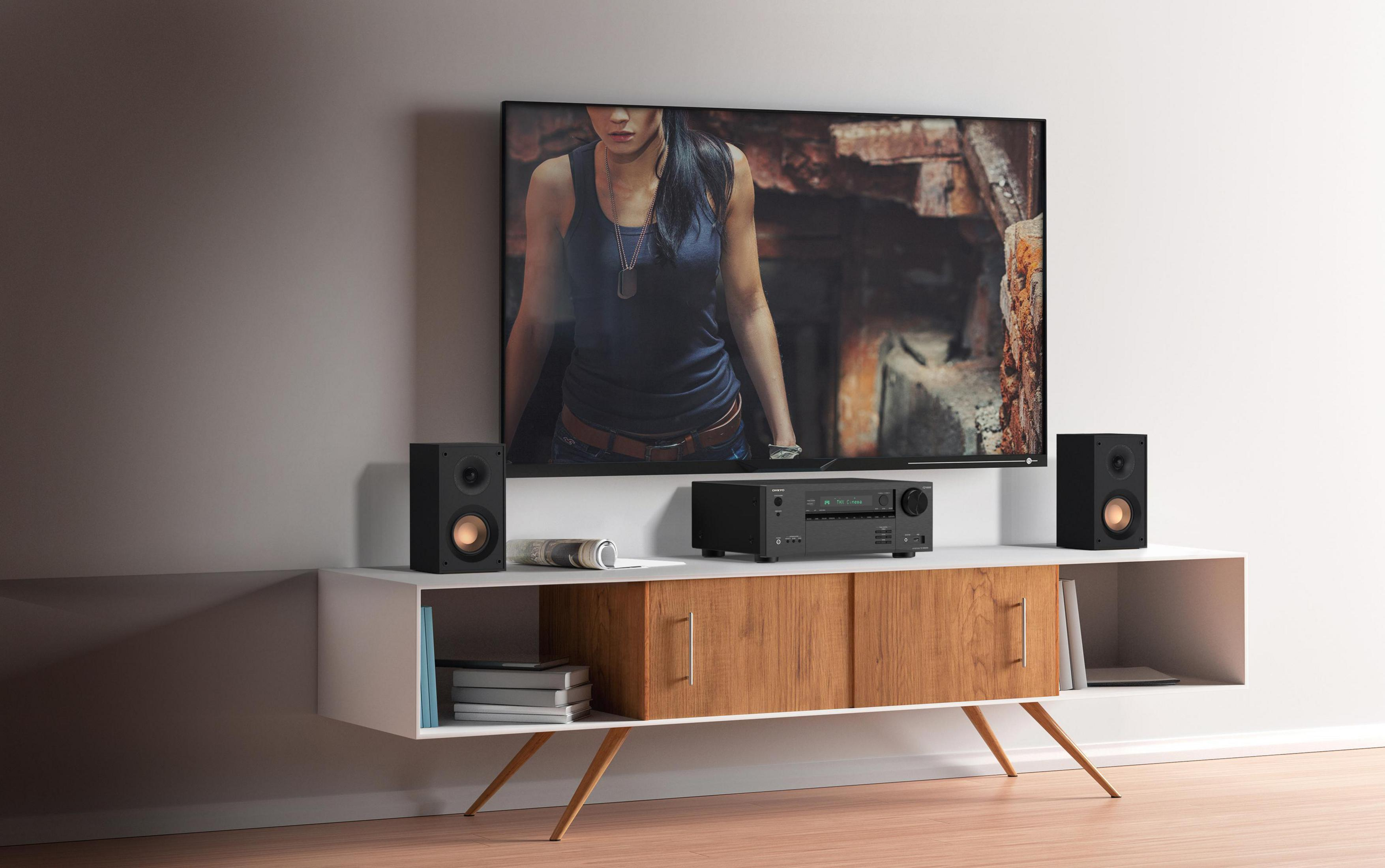 Konfiguracja rozrywki: telewizor, głośniki, odbiornik na szafce. Na ekranie scena filmowa.