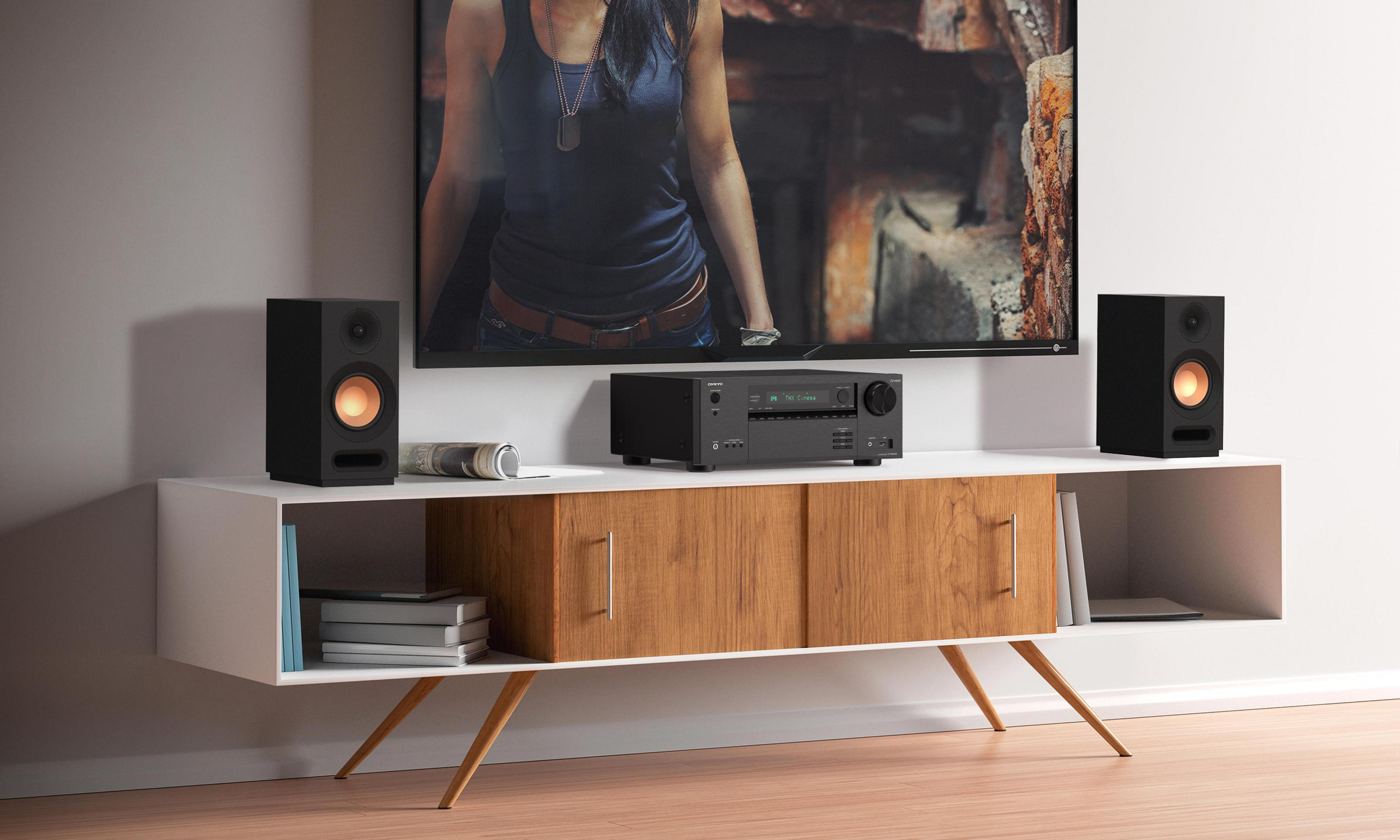 Aranżacja salonu z telewizorem, głośnikami i konsolą multimedialną. Tło: biała ściana.