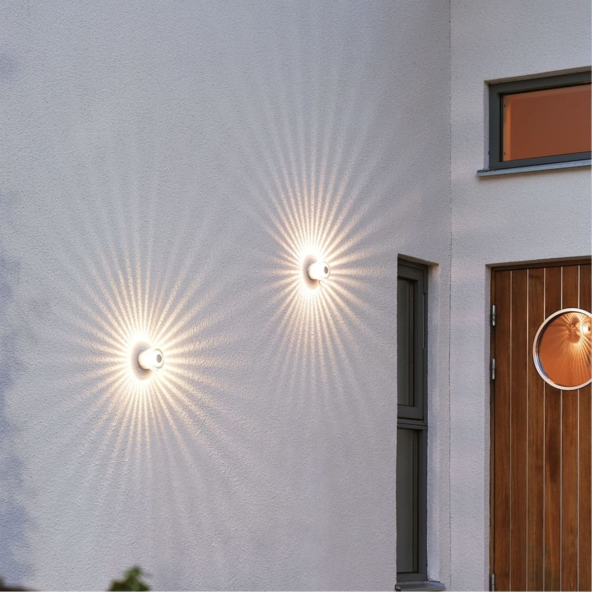 Muro esterno con due lampade da parete che emettono motivi di luce radianti.