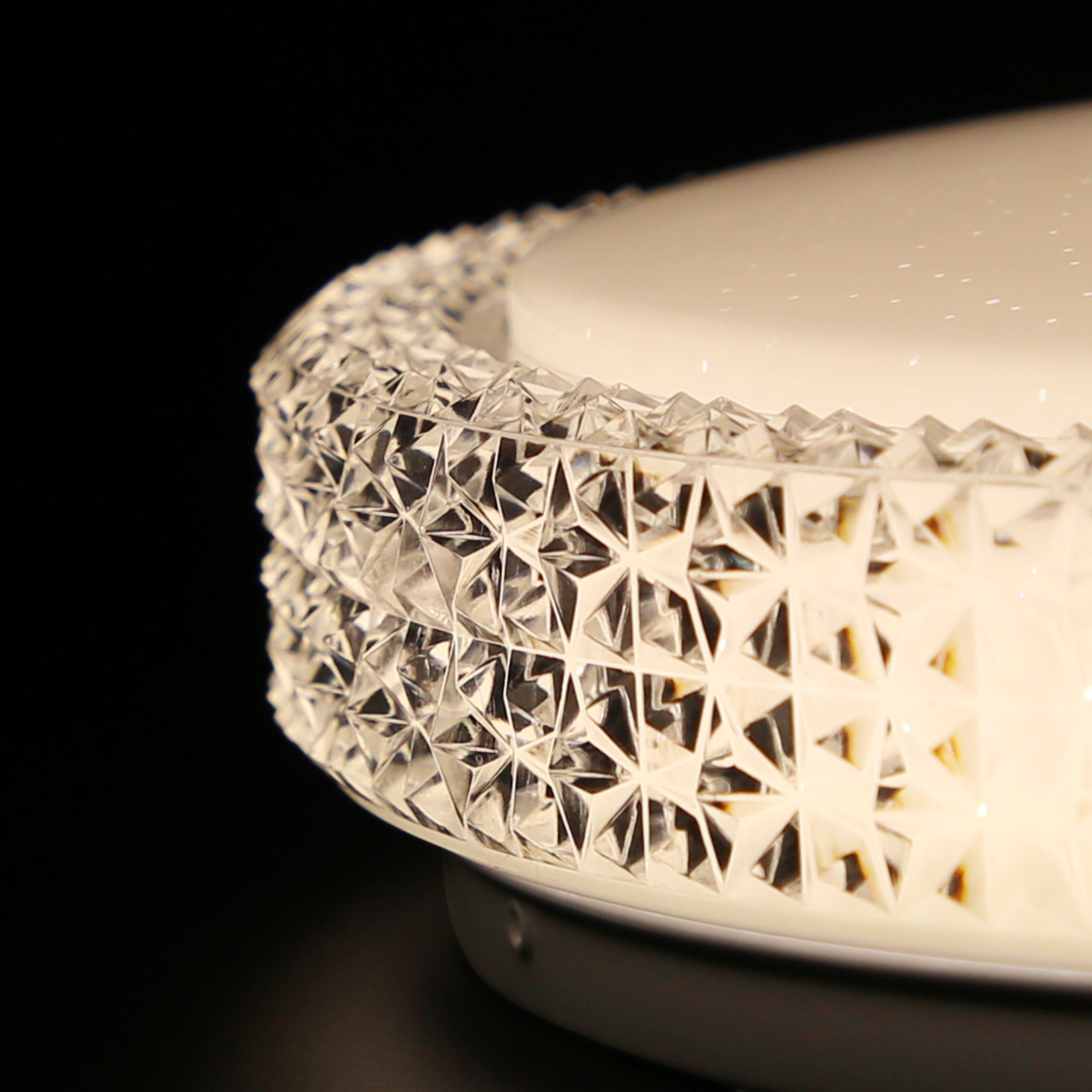 Primer plano de una lámpara de techo redonda con borde texturizado similar a cristal y superficie interior blanca.