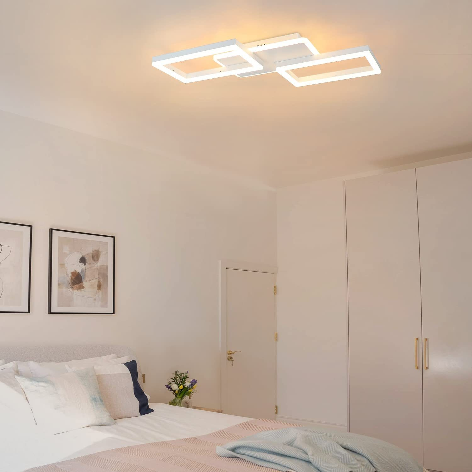 Schlafzimmer mit weißer Deckenleuchte. Weiße Wände, Bett mit Kissen und zwei gerahmte Bilder an der Wand.